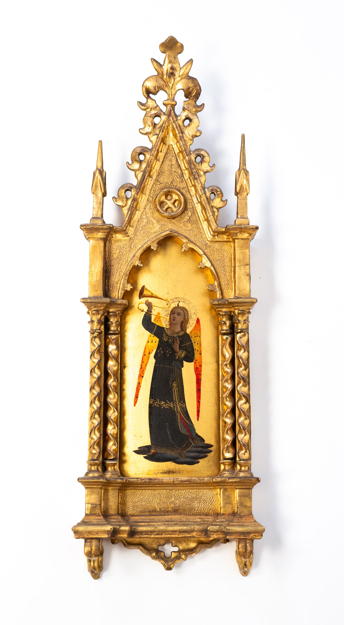 AFTER FRA ANGELICO (ITALIAN, 1395-1455) TEMPERA AND GILT ON PANEL OF AN ANGEL HOLDING A TRUMPET IN: Italy, ca. 1900. Tempera and gilt on panel. Depicting an angel with wings in a black gown holding a trumpet aloft, housed in an ornately carved gold leaf Gothic frame. 22.5"h. 7.5"w.Provenance: From t