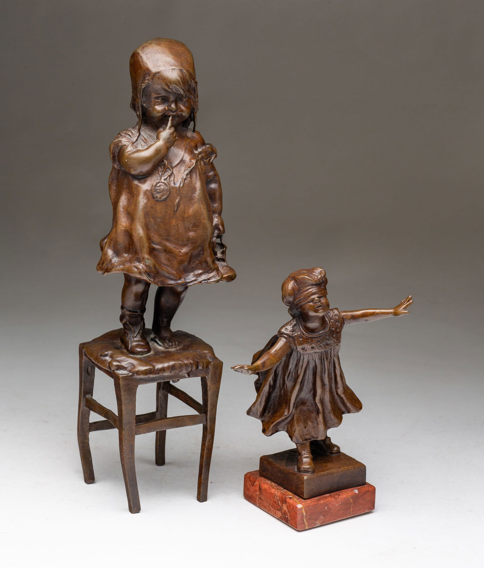 TWO DIMINUTIVE BRONZE SCULPTURES, INCL. JUAN CLARA AYATS (SPANISH-AMERICAN, 1875-1958) AND G. FERRAD: 20th Century. Standing young girl on a stool with a shoe in her hand by Juan Clara Ayats (Spanish-American, 1875-1958). Signed. 13"h. 3.25"w. 3.5"d. And a blindfolded young girl wearing a dress and wi