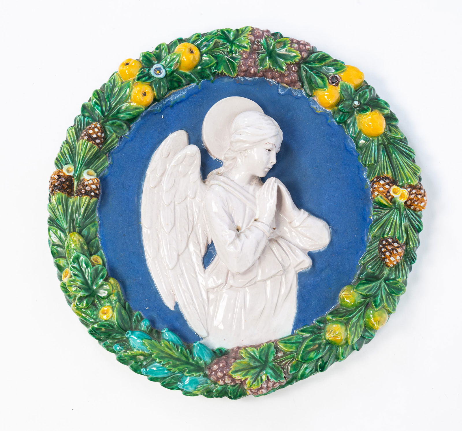 AFTER LUCA DELLA ROBBIA (ITALIAN, 1399-1481) CANTAGALLI GLAZED TERRACOTTA RELIEF WALL ROUNDEL OF AN: Italian (Florence), 20th Century. Glazed terracotta. Made by Cantagalli. Of circular form, depicting a praying angel and having a fruit and pinecone border, with maker's marks on verso. 16"d. 2"d.Prov