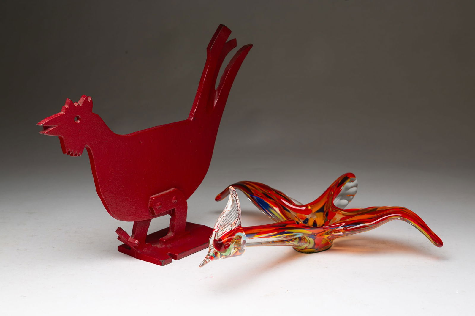 TWO DECORATIVE BIRDS, INCL. ART GLASS EXAMPLE.: American, 20th Century. A cast iron painted roadrunner boot scraper in red paint. 10.75"h. 13"w. And a blown glass long-necked bird dish. Spread wing bird with long neck and tail feather with small bo