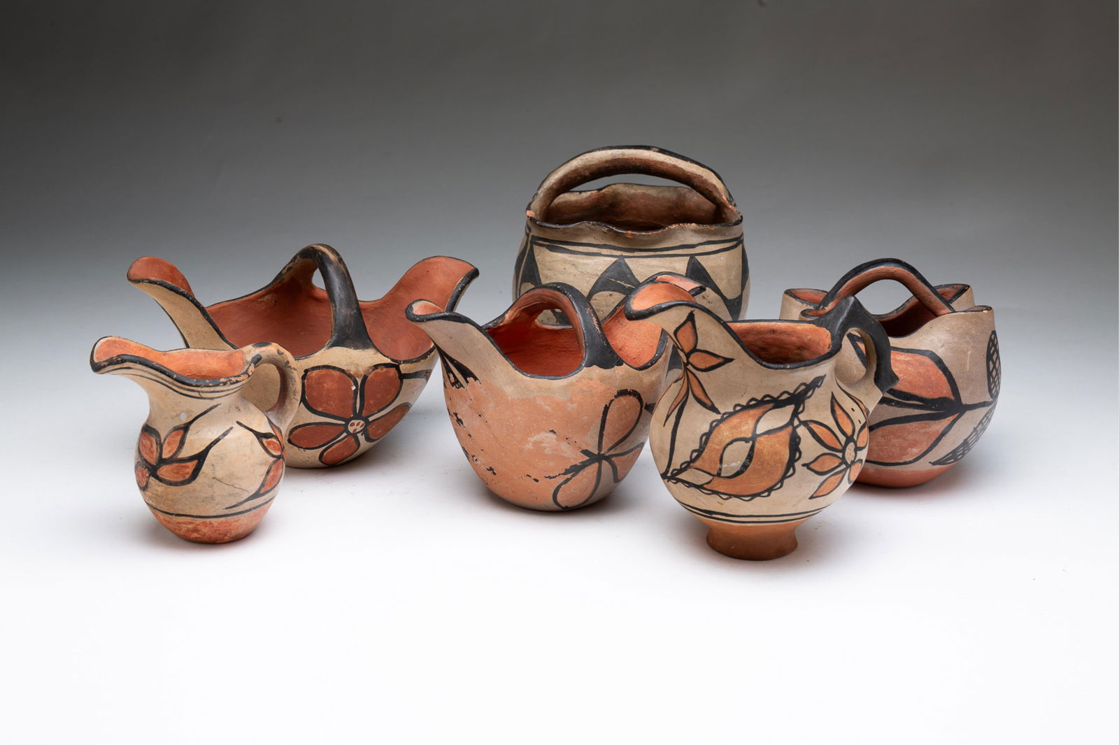 SIX HANDLED NATIVE AMERICAN PUEBLO DECORATED POTTERY VESSELS.: Native American, Early 20th Century. Including two handled pitchers, 4"h. and 5"h., two handled spherical bowls with ruffled rims, 5"h. and 6"h., and two handled double spouted bowls, 4.5"h. and 5"h.