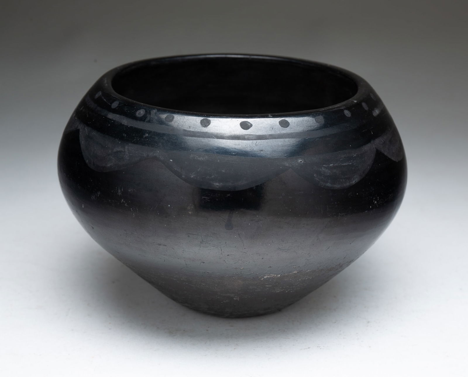 DONICIA TAFOYA (SAN ILDEFONSO PUEBLO, 1912-1979) BLACKWARE POTTERY BOWL.: Donicia Tafoya (San Ildefonso Pueblo, 1912-1979), Mid-20th Century. Of ovoid form decorated with dots, lines, and scallops beneath rim, signed on underside. 4.5"h. 6.75"d.