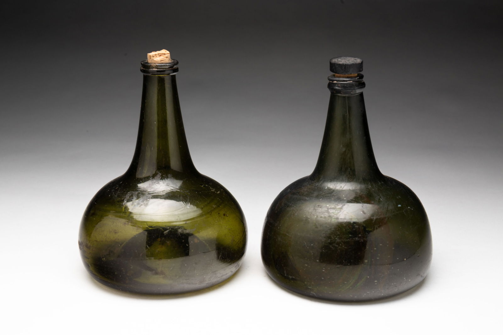TWO EUROPEAN FREE BLOWN OLIVE GREEN GLASS ONION BOTTLES.: European, 18th Century. Applied glass lips and deep push ups with broken pontils. 6.5"h. and 7"h.Provenance: From the Lifetime Collection of the late Ken Hanna (Chester, New Jersey).