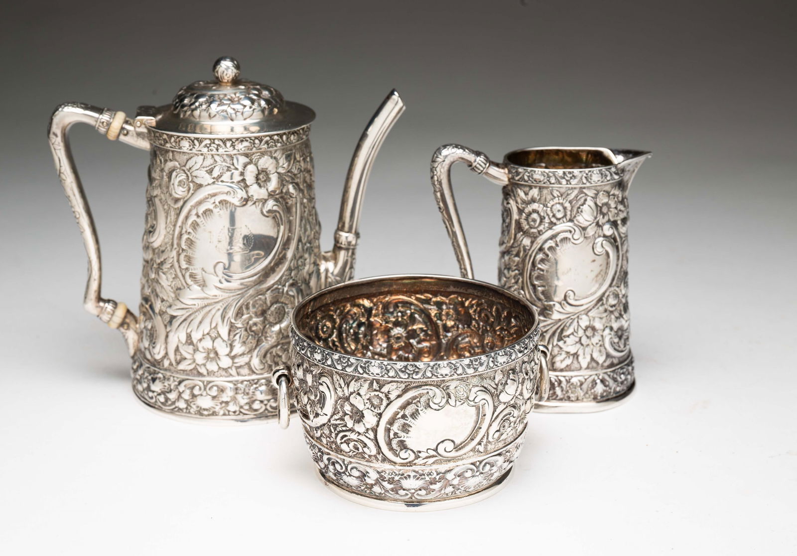 TIFFANY AND CO. STERLING SILVER REPOUSSE INDIVIDUAL TEA SERVICE.: American, 20th Century. Includes an individual tea pot with insulators, creamer and handled waste bowl. Wonderful floral repousse motif. Teapot, 5.5"h. Approximately 21.8 ozt.Provenance: From the Life