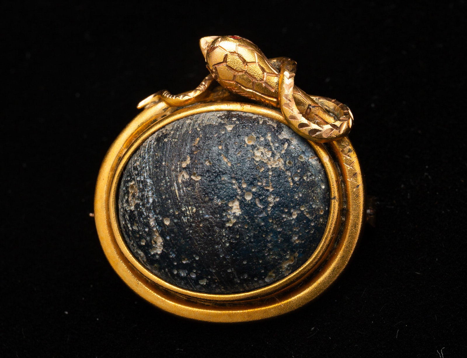 ITALIAN GOLD AND BASALT STONE SNAKE MOTIF BROOCH.: Italy, 19th Century. Oval brooch in gold set with a basalt stone to center and a snake wrapped around it. Back marked "H.H. Mayer" and "Pompeii, Feb. 11, 1908". Approximately 0.75"h. 1"w.Provenance: F