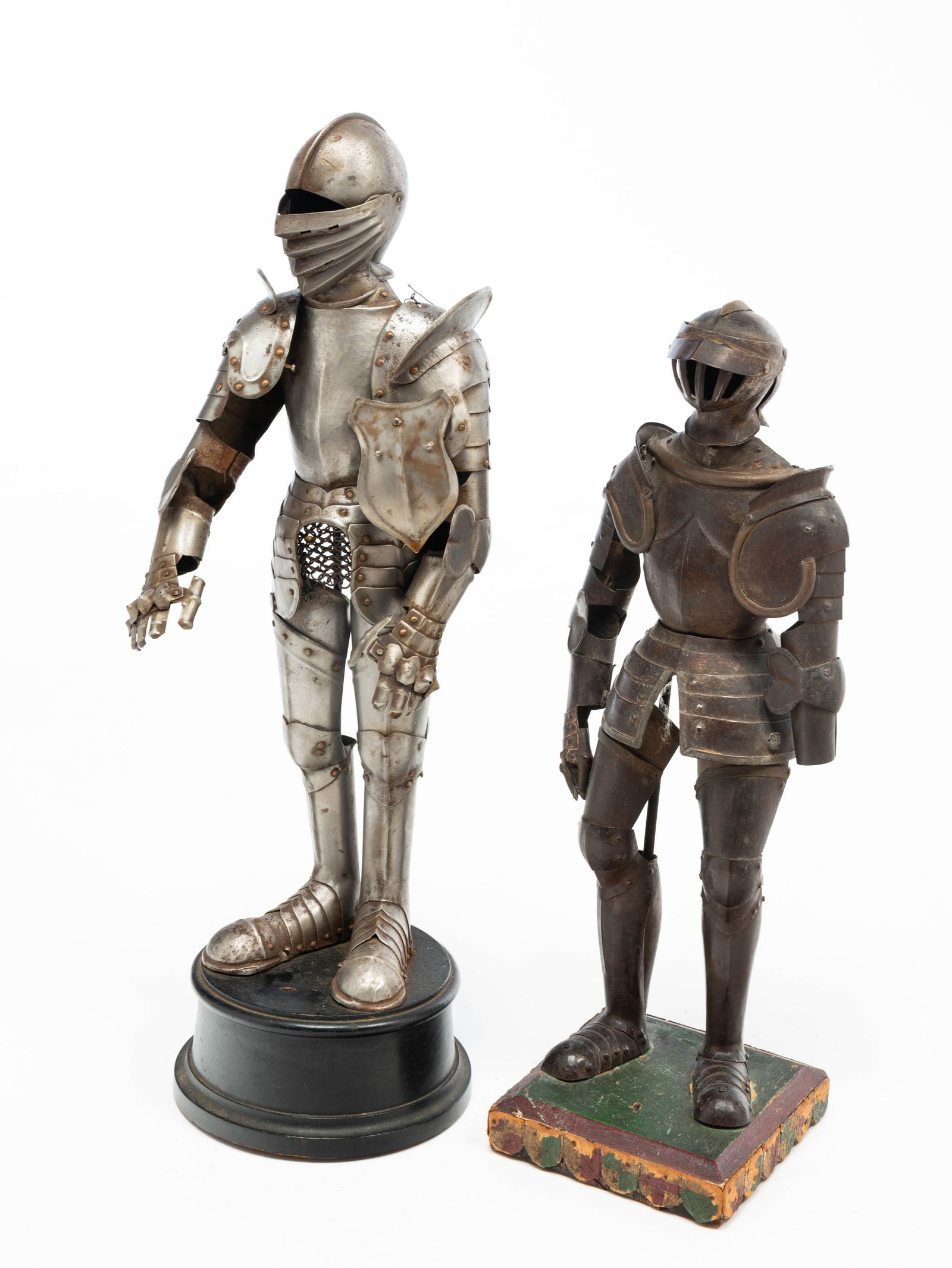 TWO TIN DIMINUTIVE FULL KNIGHT SUITS OF ARMOR.: American or European, Early 20th Century. Standing knights with helmets, chest plates, sleeves, and leg covers. On painted wooden bases. From 15"h. to 18"h.Provenance: From the Lifetime Collection of