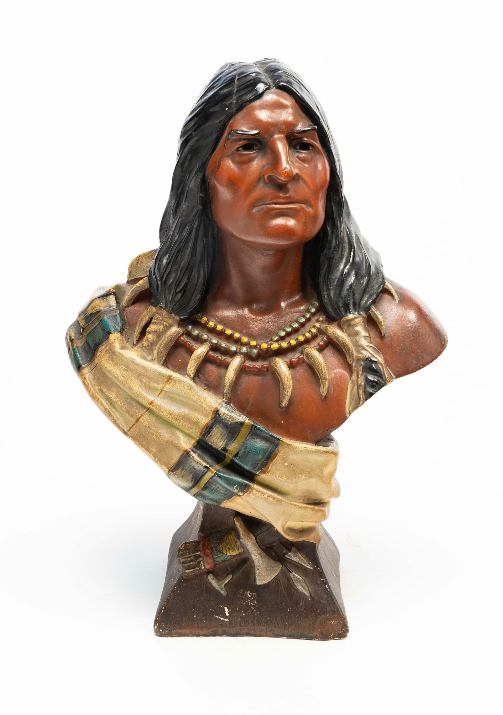 PLASTER BUST OF A NATIVE AMERICAN.: American, Early 20th Century. Polychrome painted plaster bust of a Native American with long hair tied at ends, several beaded necklaces and a sash, with an axe, arrows, and a bag at base. 18"h. 12"w.