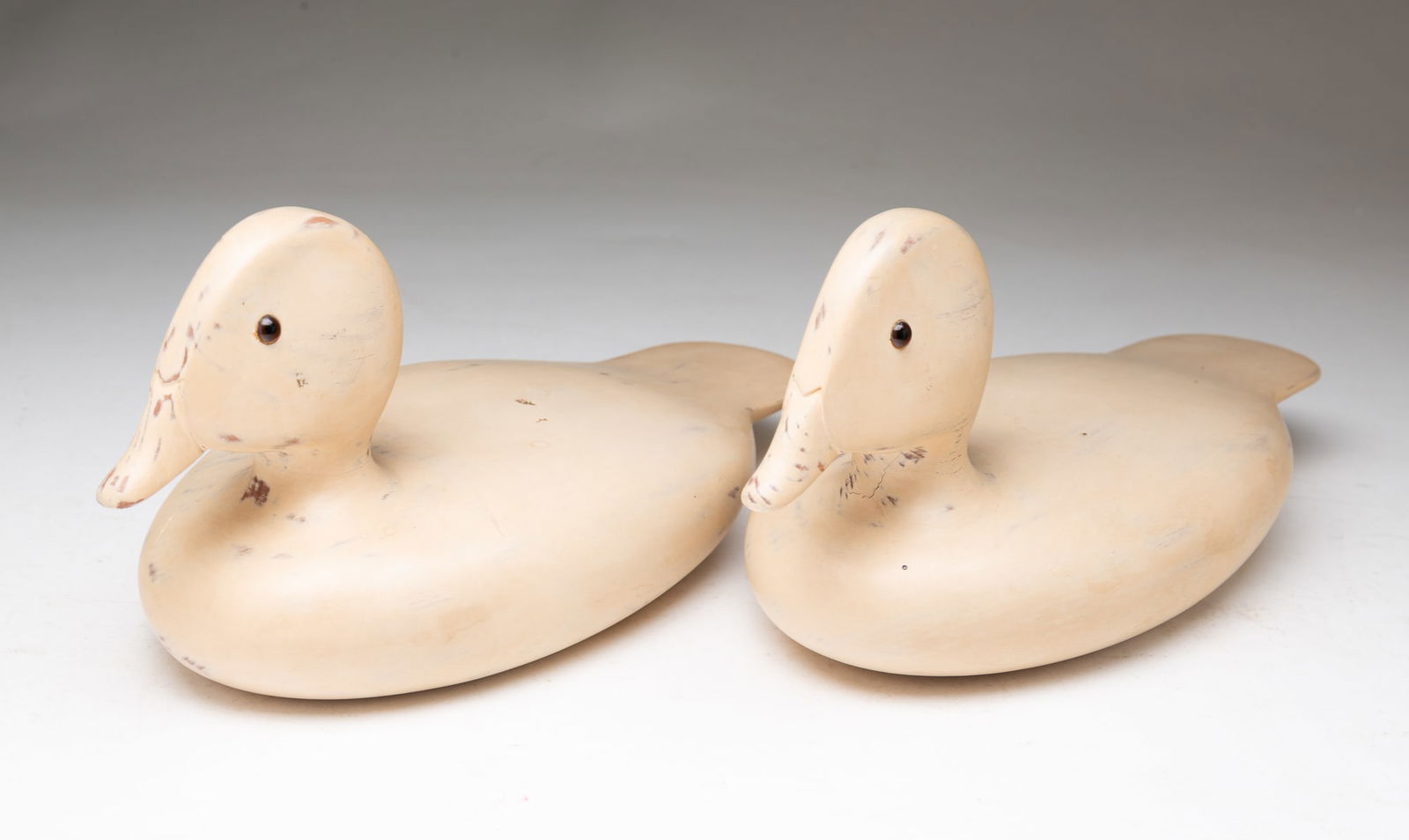 PAIR OF PAINTED DUCK DECOYS.: American, 20th Century. Two carved wooden decoys with thick coat of beige paint and glass eyes. 5"h. 11"l.