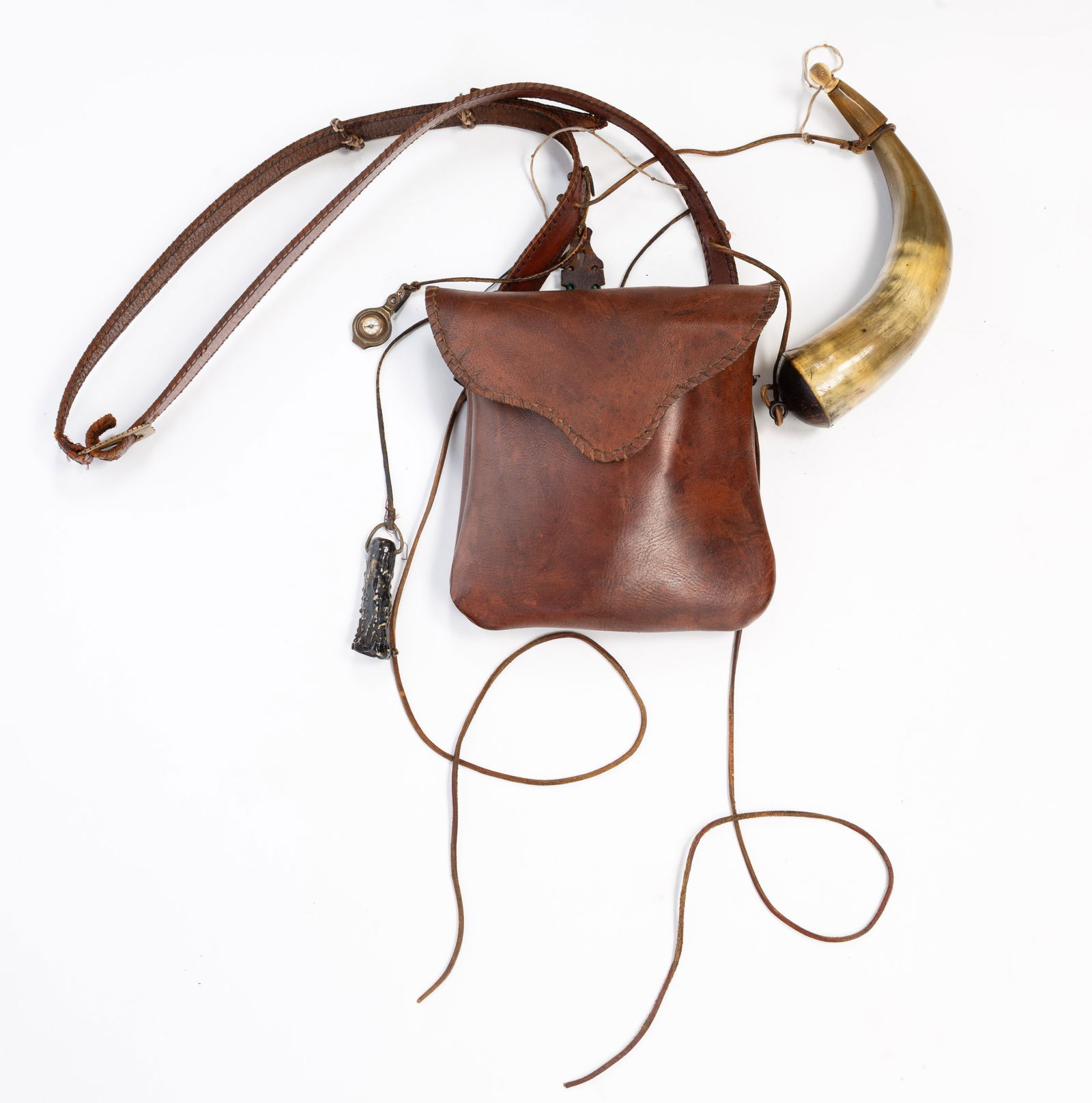 AMERICAN REVOLUTIONARY WAR REENACTORS LEATHER POUCH AND ACCOUTREMENTS.: American, 19th and 20th Centuries. Hand sewn pouch with strap. Included are a tinder box, bullet mold, spoon, powder horn, shot and powder measures, shot flasks, sharpening stone and a compass.
