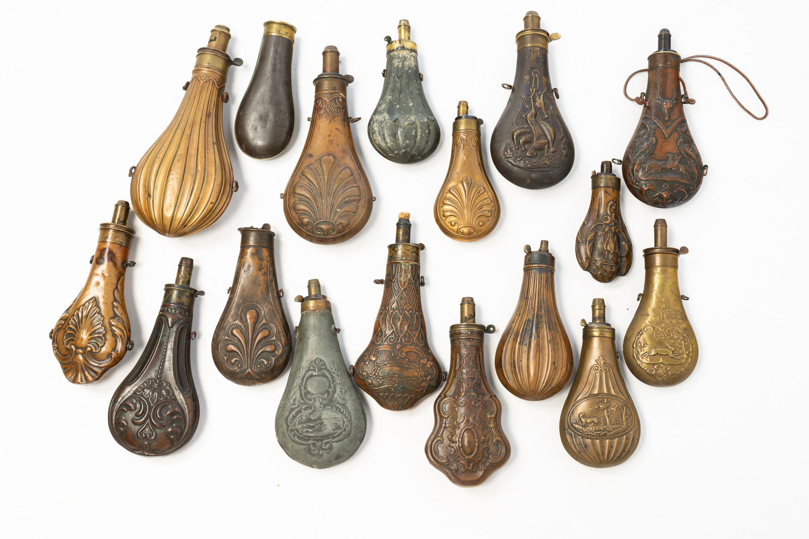 GROUP OF SEVENTEEN EMBOSSED BRASS, COPPER, AND METAL SHOT FLASKS.: 19th Century. Brass, copper, and metal. Including six with animals or hunting scenes, ten with decorative motifs, and one plain example. Largest is 10"l.