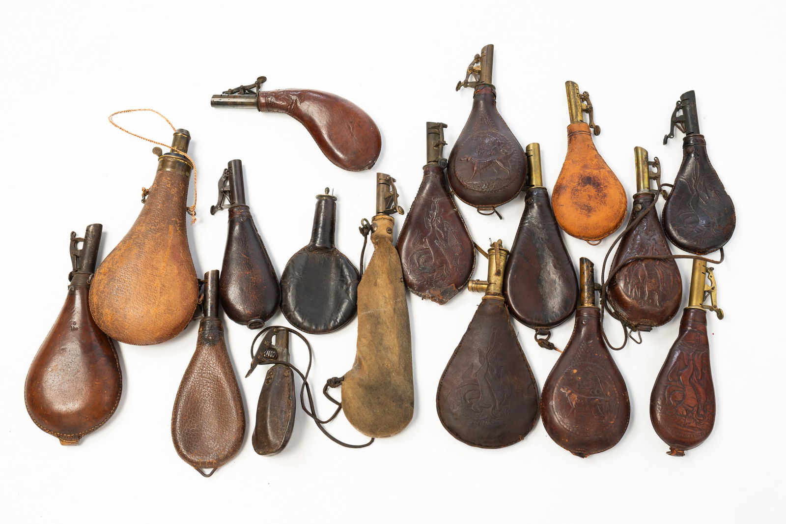GROUP OF SEVENTEEN LEATHER SHOT FLASKS, INCL. JAMES DIXON & SONS.: 19th Century. Leather, brass, and metal. Comprising eight embossed leather examples, one of which is marked "JAMES DIXON & SONS" and nine plain leather flasks. One spout is stamped "AM FLASK & CAP CO.