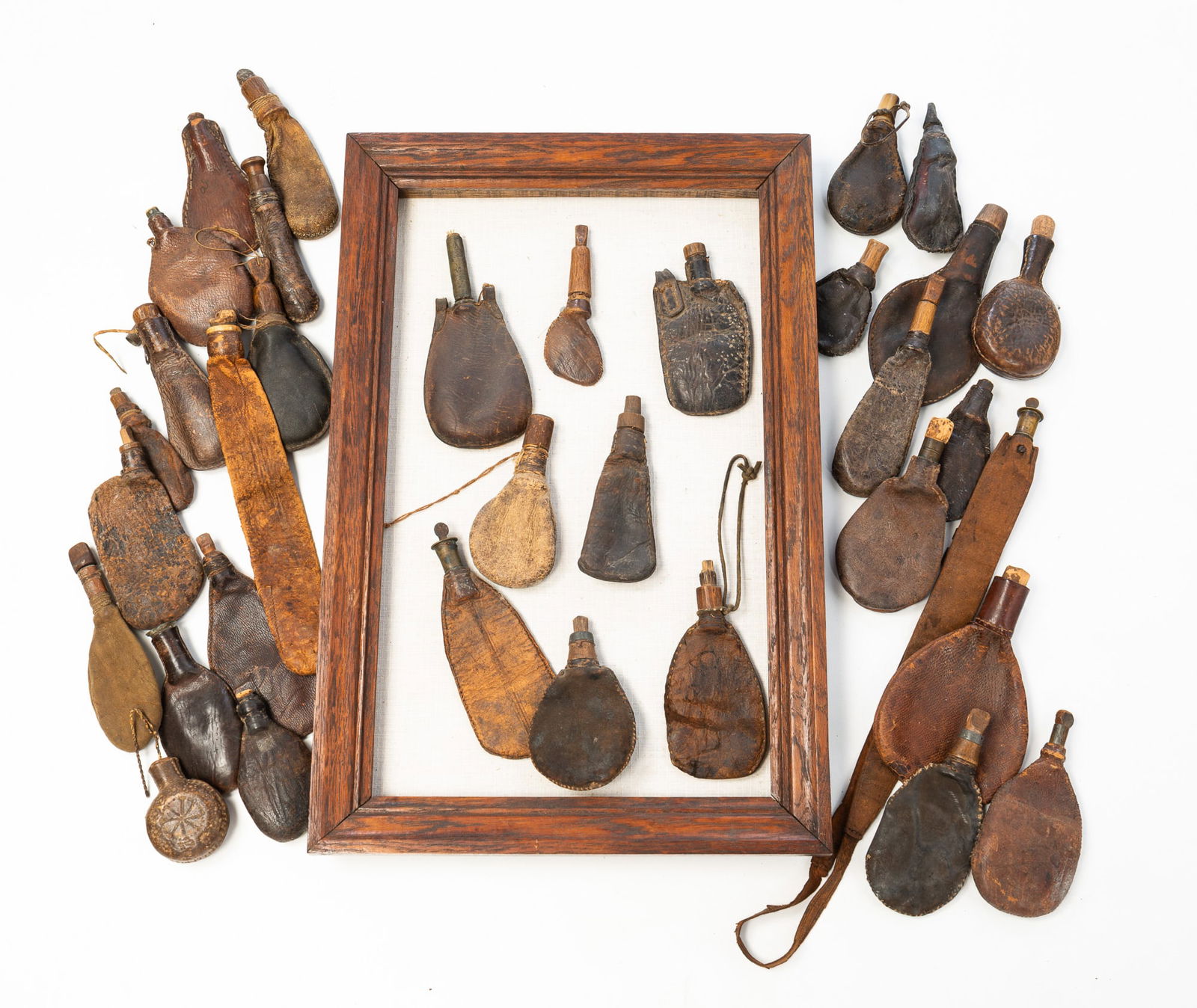 COLLECTION OF THIRTY-FOUR LEATHER SHOT FLASKS.: American, 19th Century. Leather, wood, horn, brass, and glass. Most with wood stoppers while one has a horn example, two have brass collars, and another has a glass spout insert. Eight are presented i