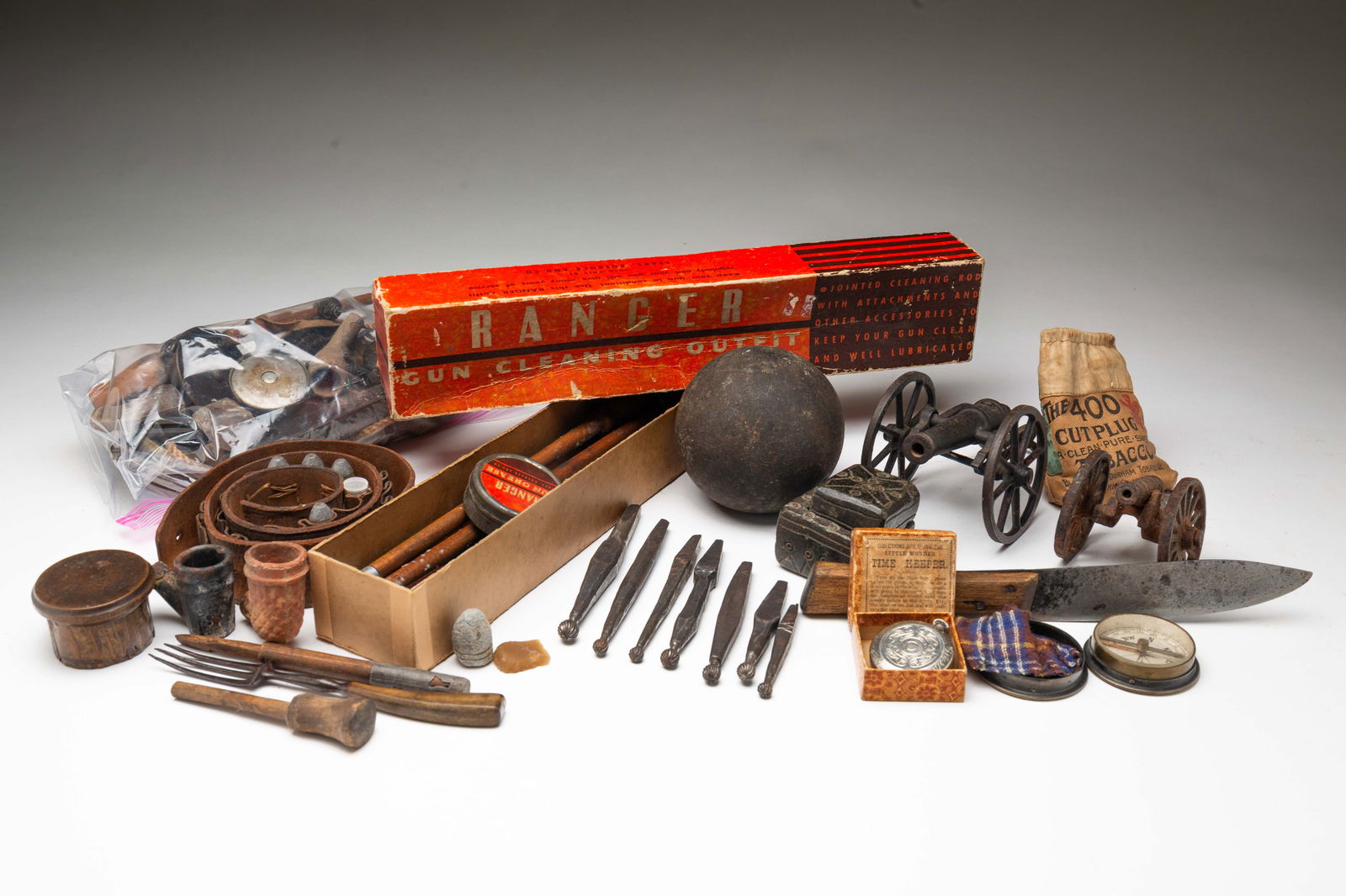 AN ECLECTIC GROUP.: American, 19th and 20th Centuries. Cannon ball, battlefield dug bullets, gun cleaning kit, two cast iron toy cannons, clay trade pipes, rifle flints, measures, gun lock parts, bullet mold cherries, ri