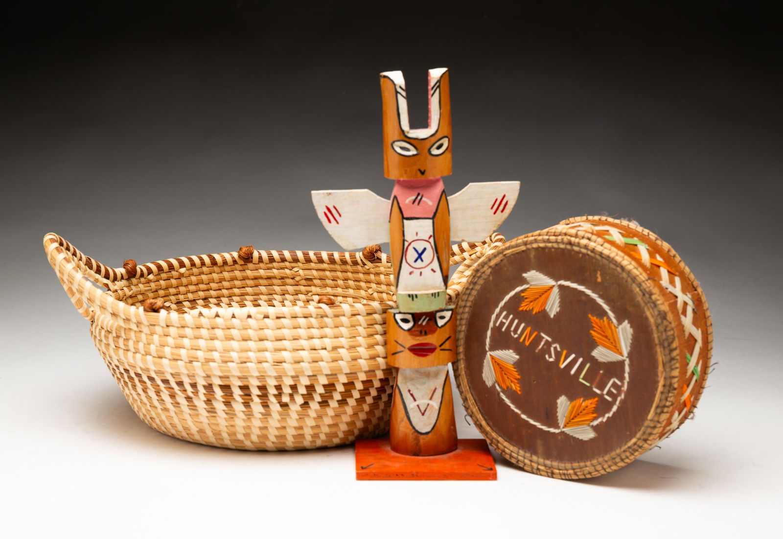 CARVED TOTEM POLE AND TWO BASKETS.: American, 20th Century. Cherokee craved totem pole with two stacked figures, 18"h. South Carolina sweetgrass basket with two handles, 13.5"d. And a porcupine lidded basket with Huntsville lid, 6"d.