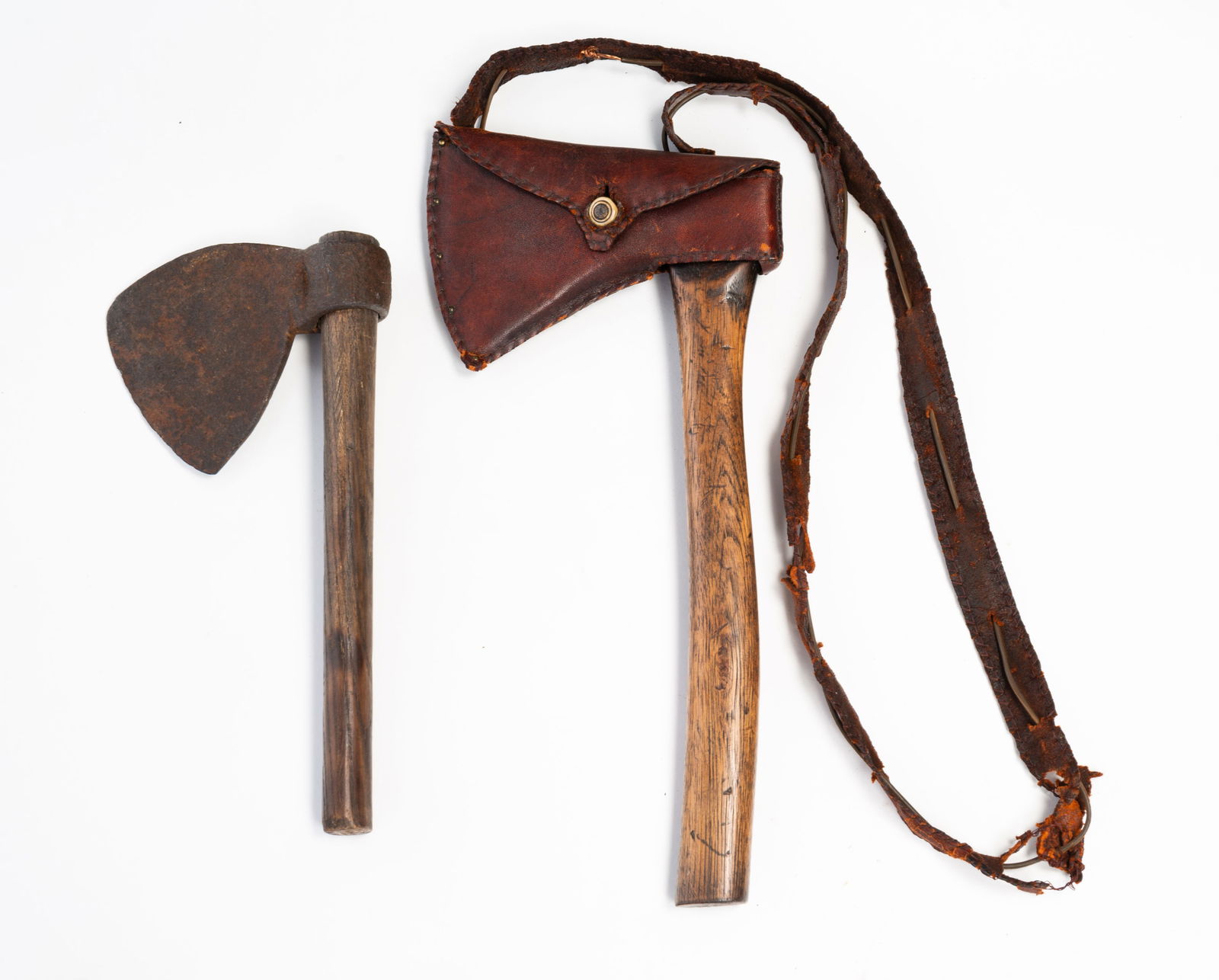 TWO AMERICAN FORGED IRON HATCHETS.: American, Early 19th Century. The larger has an oak handle and leather hand made cover and carrying strap. 14''h. 6.75"w. And the second also has an handle and unusually shaped blade. 11.75"h. 6"w.