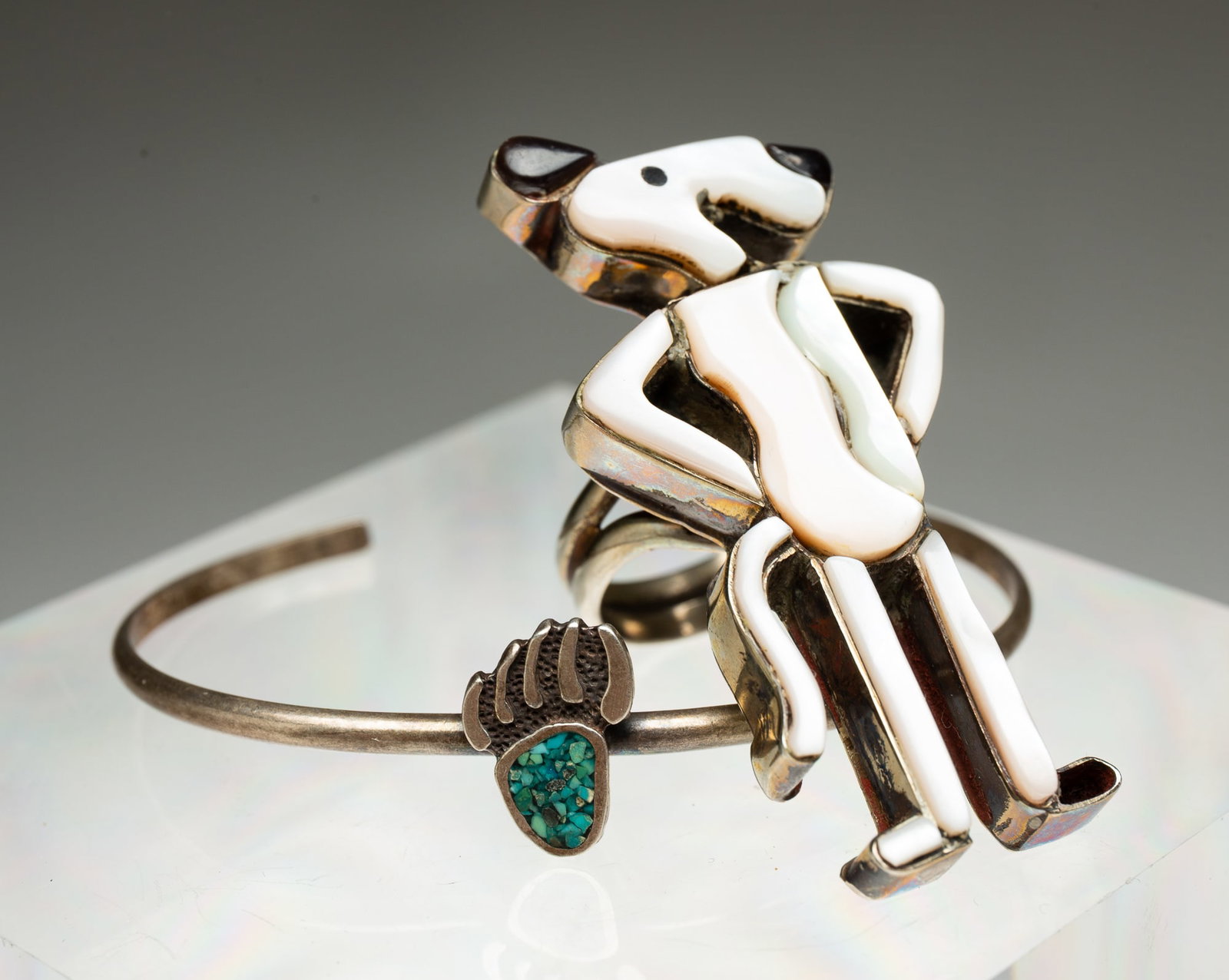 NATIVE AMERICAN ANIMAL MOTIF BRACELET AND RING.: Native American, 20th Century. A diminutive silver cuff with a crushed turquoise accented bear claw. 2.5"w. 1.25" opening. And a Zuni Snoopy ring comprised of Mother of Pearl and onyx. Size 8.5. Appro