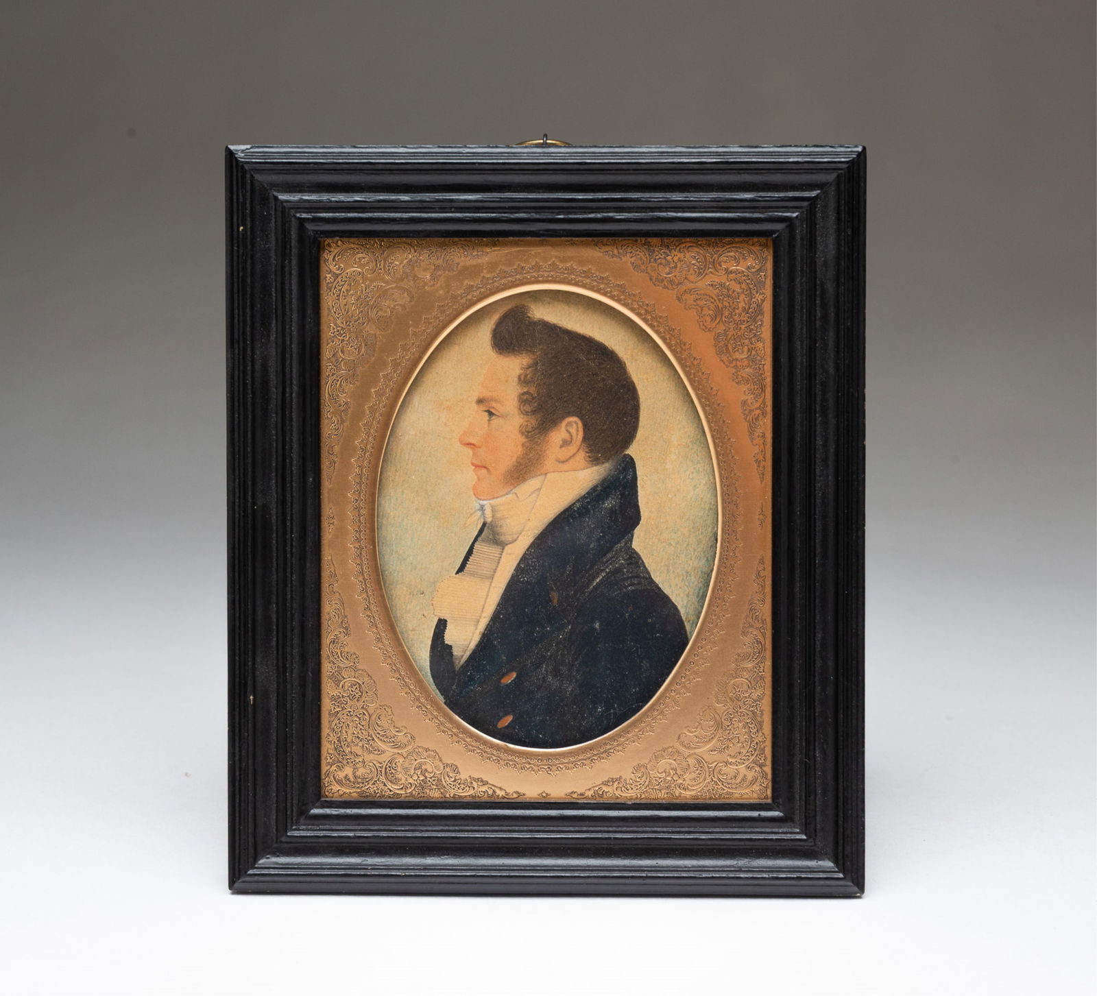 RUFUS PORTER (1792-1884) FINE MINIATURE WATERCOLOR PORTRAIT OF A YOUNG NEW ENGLAND GENTLEMAN.: American, 19th Century. On paper. Young man with curly, upswept hair and large sideburns wearing a high-collared white shirt and tie and a navy blue coat with gold button, in a decorative oval brass m