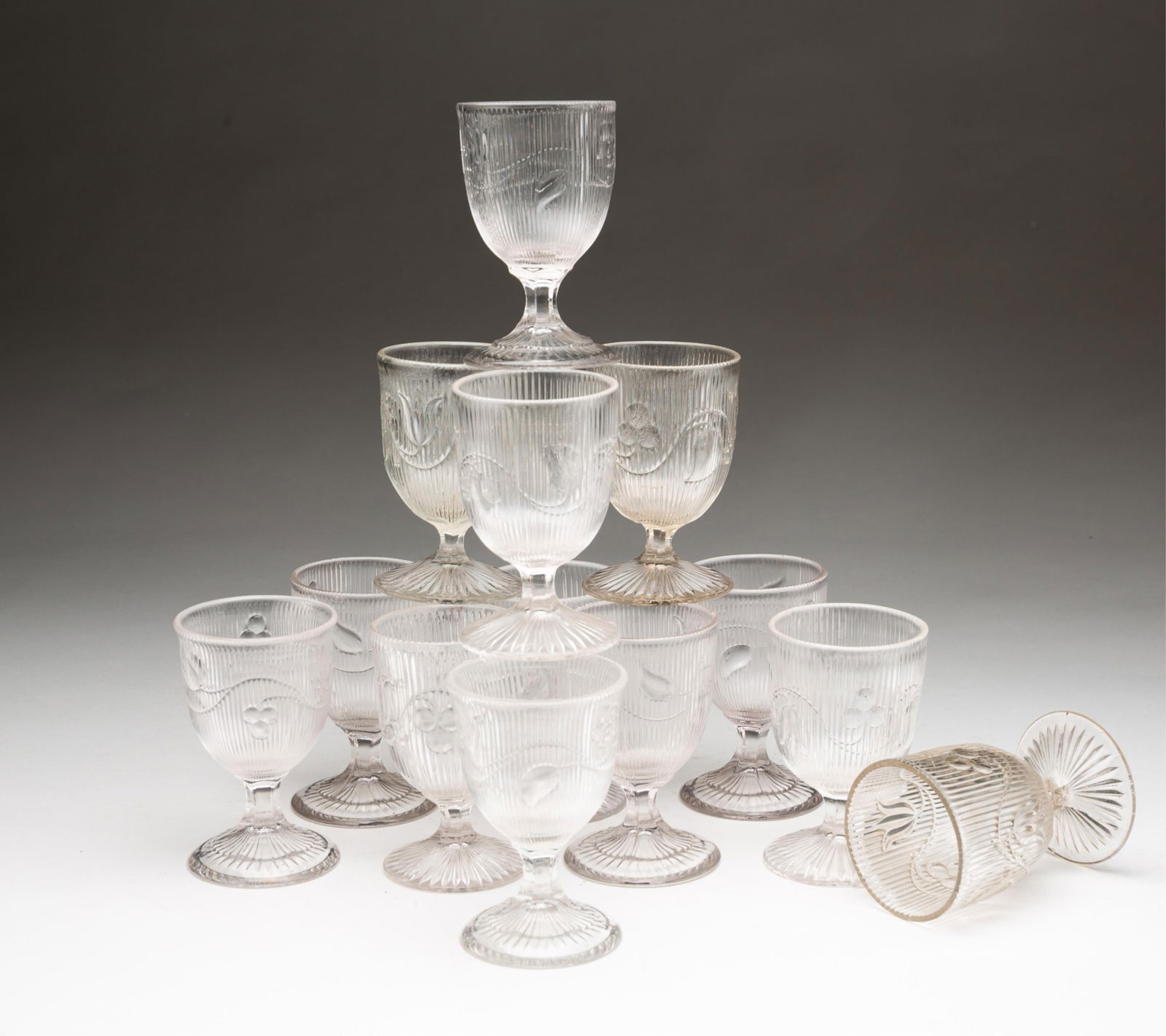 THIRTEEN BOSTON AND SANDWICH GLASS COMPANY "BELLFLOWER" EGG CUPS.: Third quarter 19th Century. Flint glass with single vine and starburst feet. Two with flared rims. 4"h.