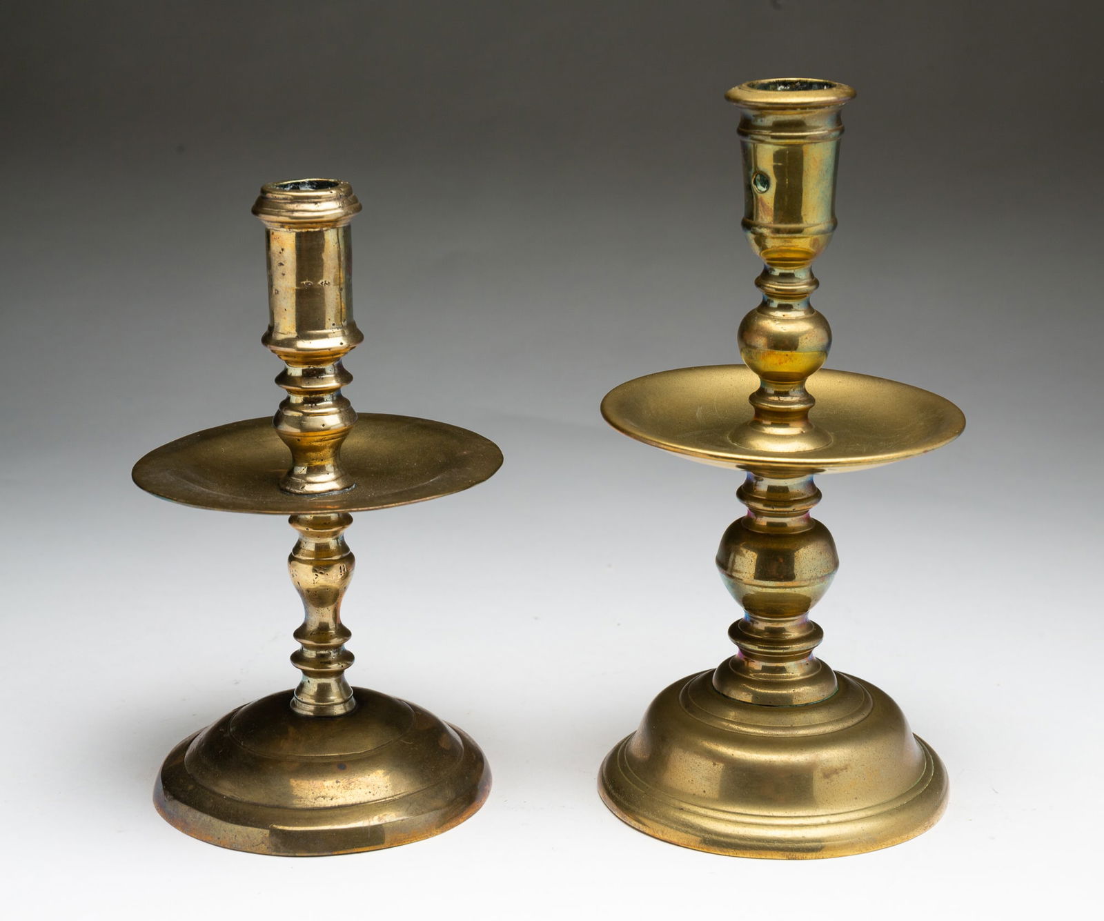 TWO EUROPEAN BRASS CANDLESTICKS.: Ca. 1700. Taller candlestick with round stepped base, baluster stem, mid-stick wax catcher and cylindrical socket with ejector holes, 8.75"h. And second with round stepped base, baluster body, mid-sti