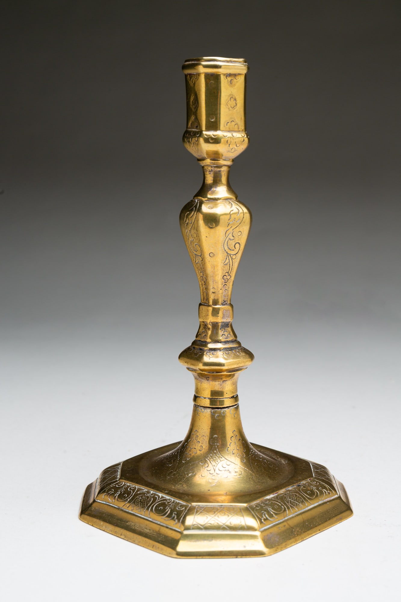 EUROPEAN ENGRAVED BRASS HUGUENOT CANDLESTICK.: Ca. 1700. Octagonal stepped base, stem and socket with decorative engraving. Remnants of old silvering to bottom. 7.5"h. 4.25"w.Provenance: From the Collection of Peggy McClard & Randy Segotta (Weare,