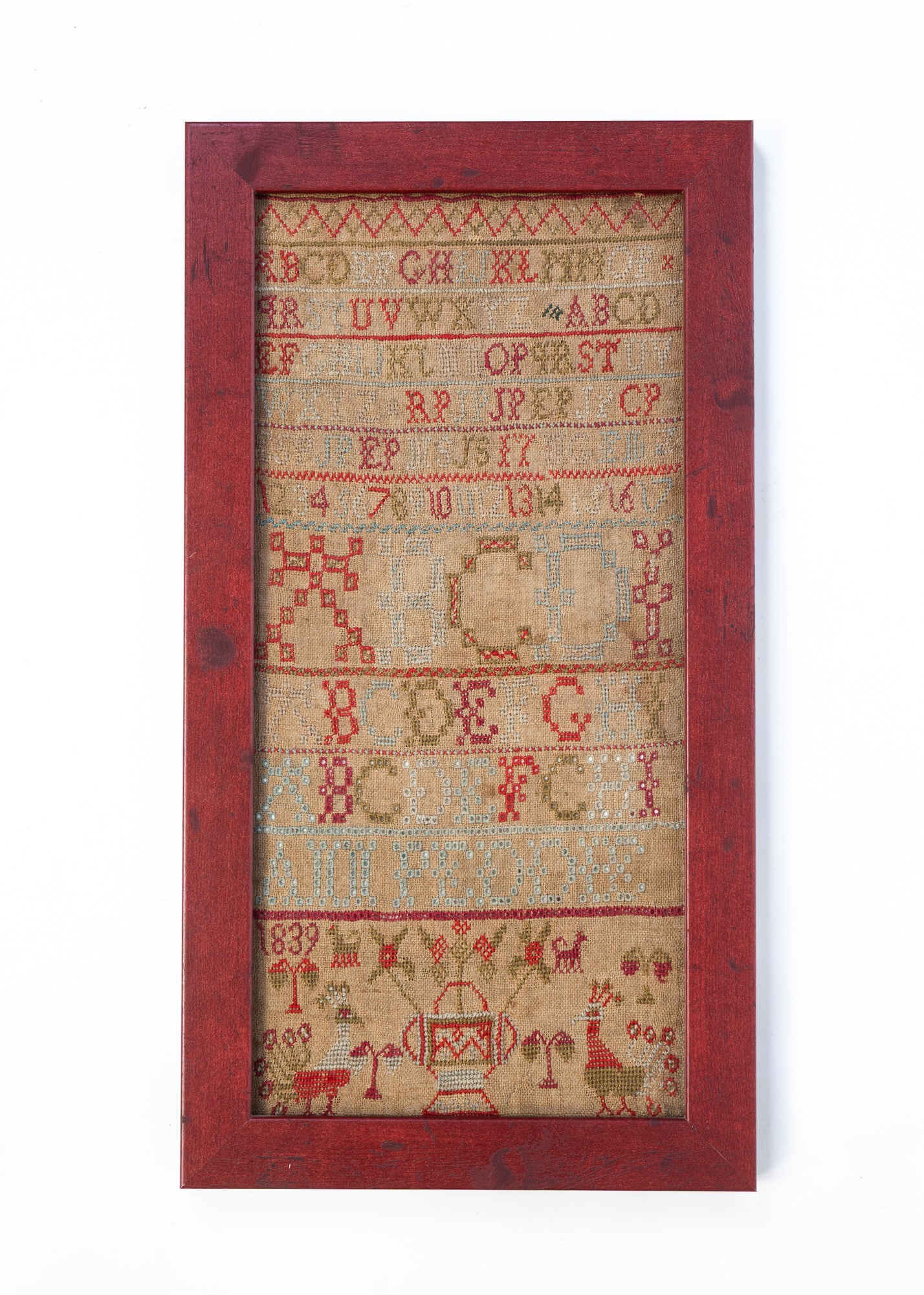 AMERICAN NEEDLEWORK SAMPLER, DATED 1839.: Polychrome silk thread on linen. Alphabet sampler in colors of red, green, tan, blue above a flowering urn flanked by dogs, and peacocks, in modern red frame. Frame, 18.75"h.Provenance: From the Colle