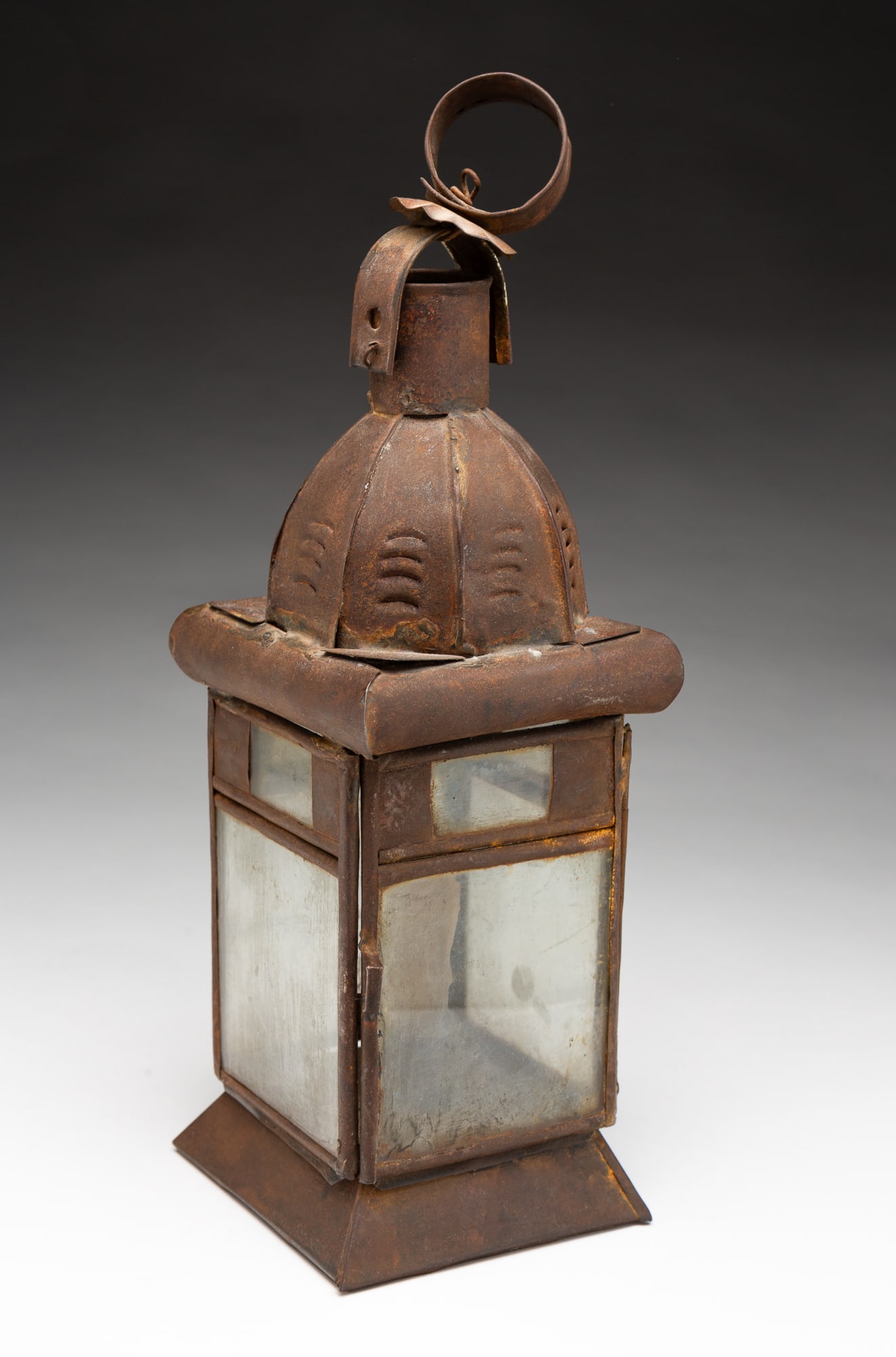 AMERICAN PUNCHED TIN AND GLASS CANDLE LANTERN.: Ca. 1800. Loop handle, punched and faceted dome top with high chimney, square body with two-panel windows, hinged door, single candle socket, and a beveled base. With handle, 12.5"h.Provenance: From t