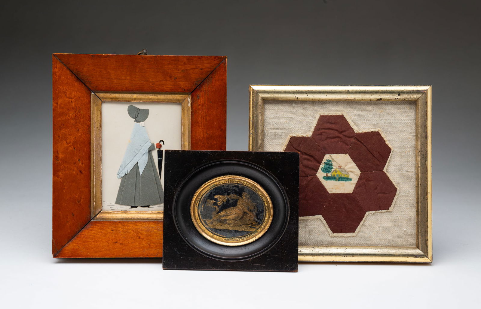 THREE DIMINUTIVE AMERICAN SCHOOL ARTWORKS, INCL. EGLOMISE EXAMPLE.: 19th Century. A quilt patch with watercolor painted house with tree in yard to the center tile with brown hexagons surrounding. Laid on linen behind glass in a period half-round gilt frame, 6.5"h. 6.7