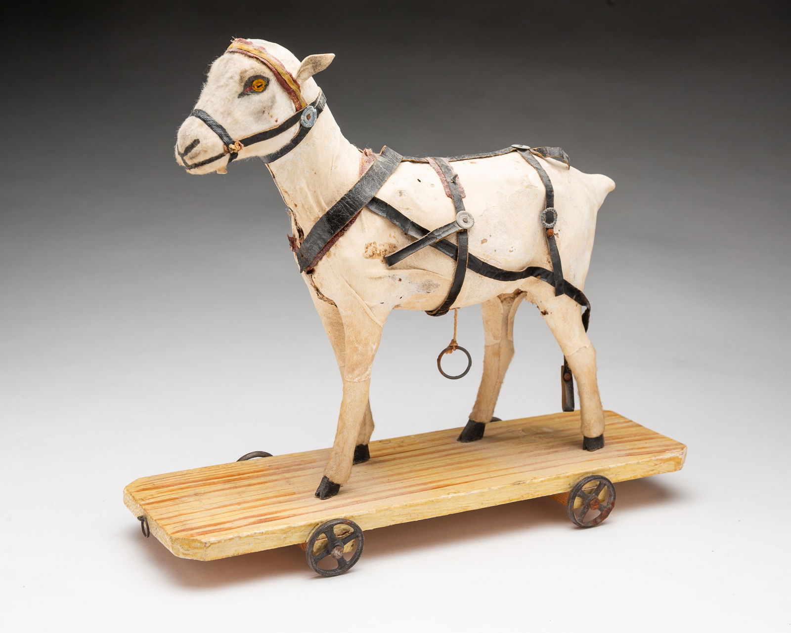 GERMAN PAPIER-MACHE AND MOHAIR GOAT PULL TOY WITH SQUEAKER.: Early 20th Century. Papier-mache body, wooden legs covered in mohair, having one glass eye and one painted eye, leather ears, and leather reins, having a pull-string on belly that makes a goat sound,