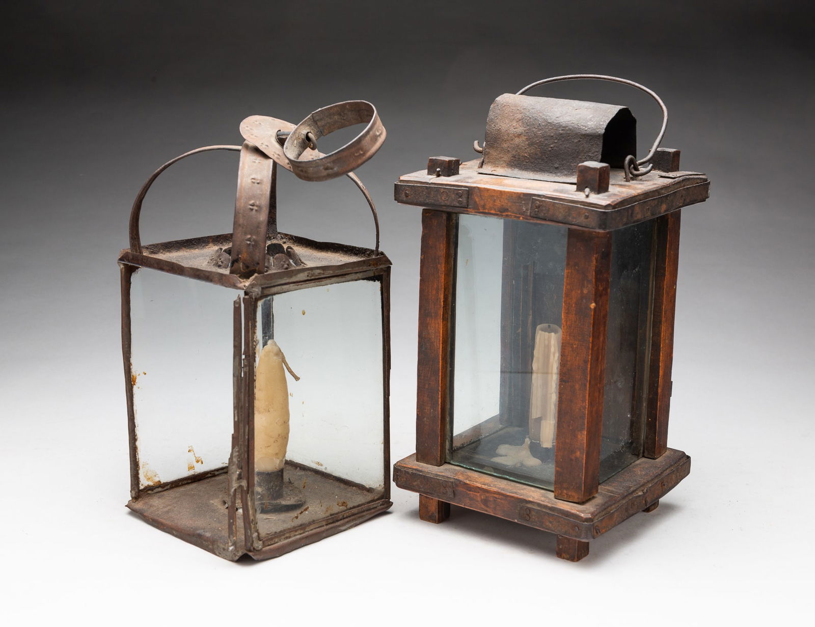 TWO AMERICAN WOOD AND METAL CANDLE LANTERNS.: Mid-19th Century. A wood-framed lantern with three glass side, wood door to back with iron strap hinges, sheet metal vent cover and bail handle, 10"h. And an iron-farmed lantern glass sides, arched to