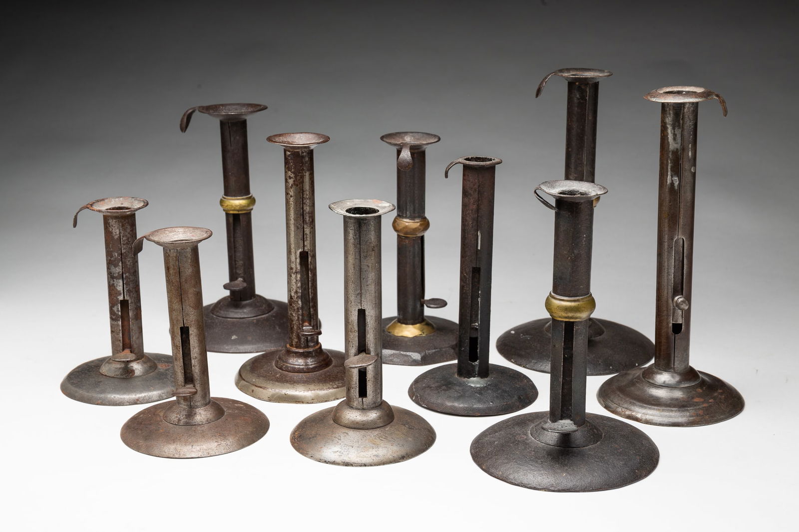 TEN HOGSCRAPER CANDLESTICKS.: 19th-20th Century. All ten have pushups. Four have brass rings, from 8.5"h. to 6.5"h. The remaining six are 8.5"h. to 5.25'h. Second tallest has push up marked "Davis".
