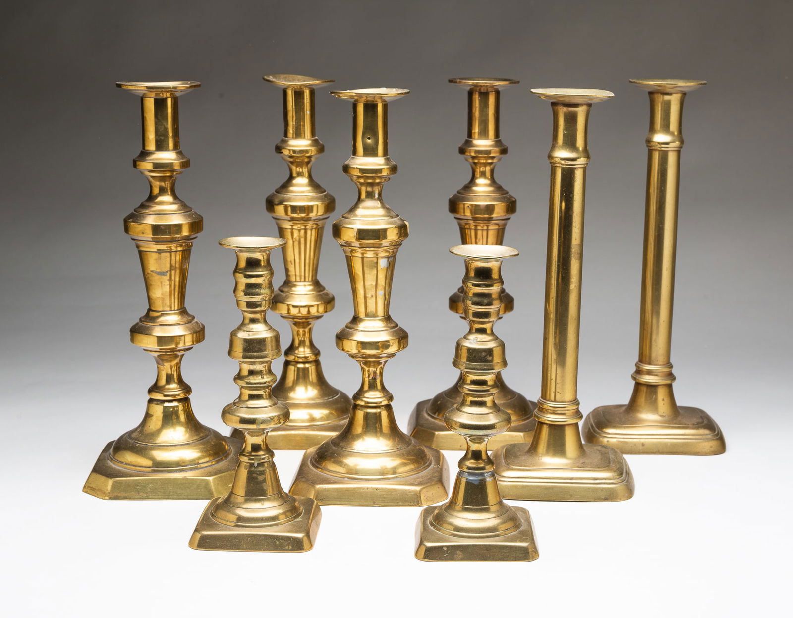 FOUR PAIRS OF AMERICAN BRASS CANDLESTICKS.: 19th Century. Two tall push-up pairs with urn forms on stems and square bases with cut corners, 12"h. Tall pair with straight stems and rectangular bases having rounded corners, 12"h. Short push-up