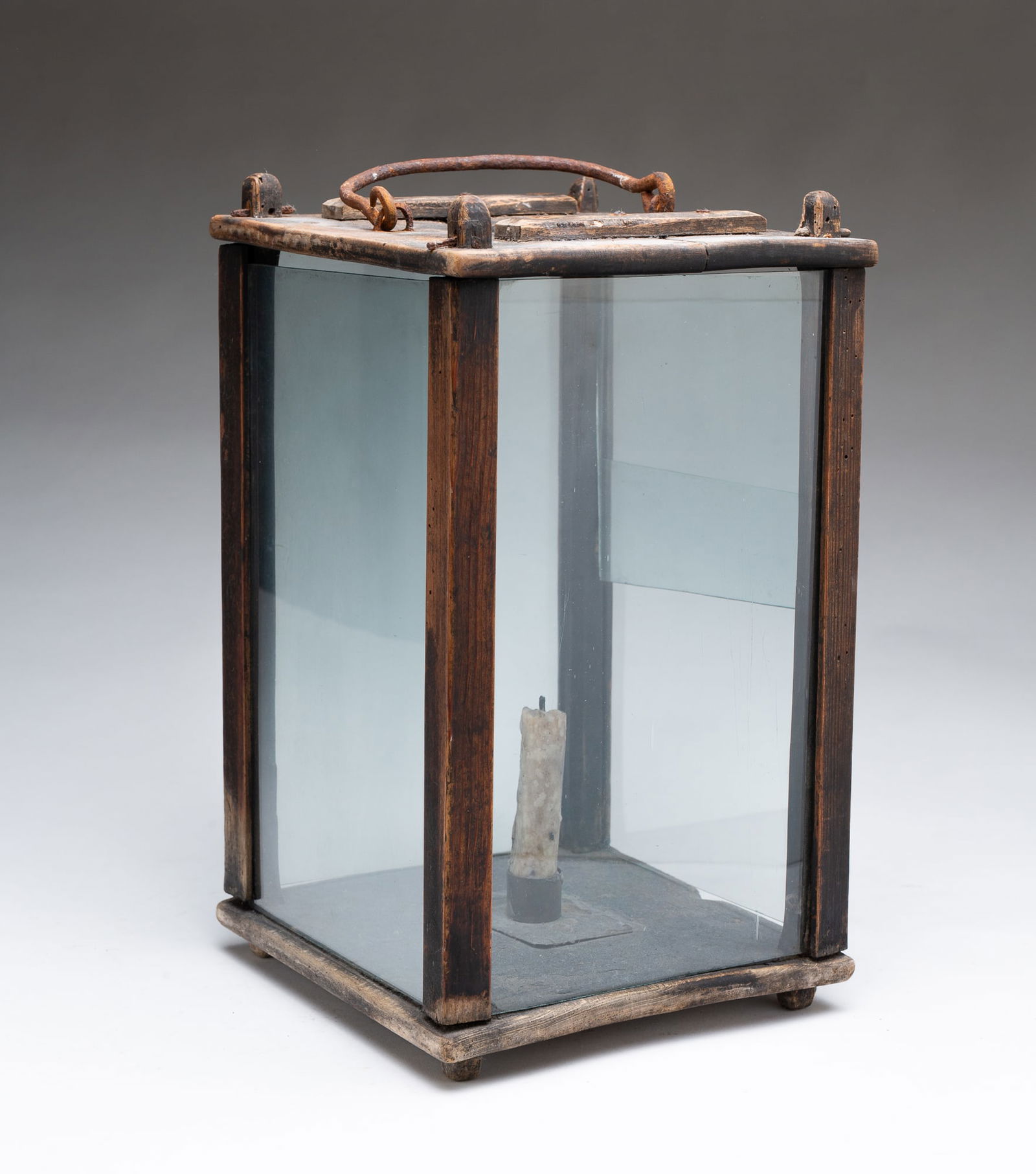 AMERICAN PINE BARN LANTERN.: Mid-19th Century. Square base and top, square corner posts, iron bale handle, four sides of glass with one sliding glass panel, single candle socket, and four feet. With handle, 15.5"h.Provenance: Fro
