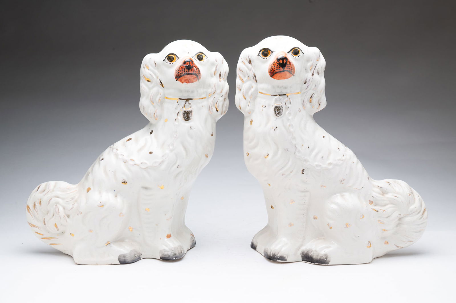 PAIR OF STAFFORDSHIRE PORCELAIN SPANIELS.: English, mid-19th Century. Seated white spaniels with yellow eyes, orange noses, and gilt highlights. 12"h.Provenance: From the Lifetime Collection of the late Deb Fisher (Lebanon, Ohio).