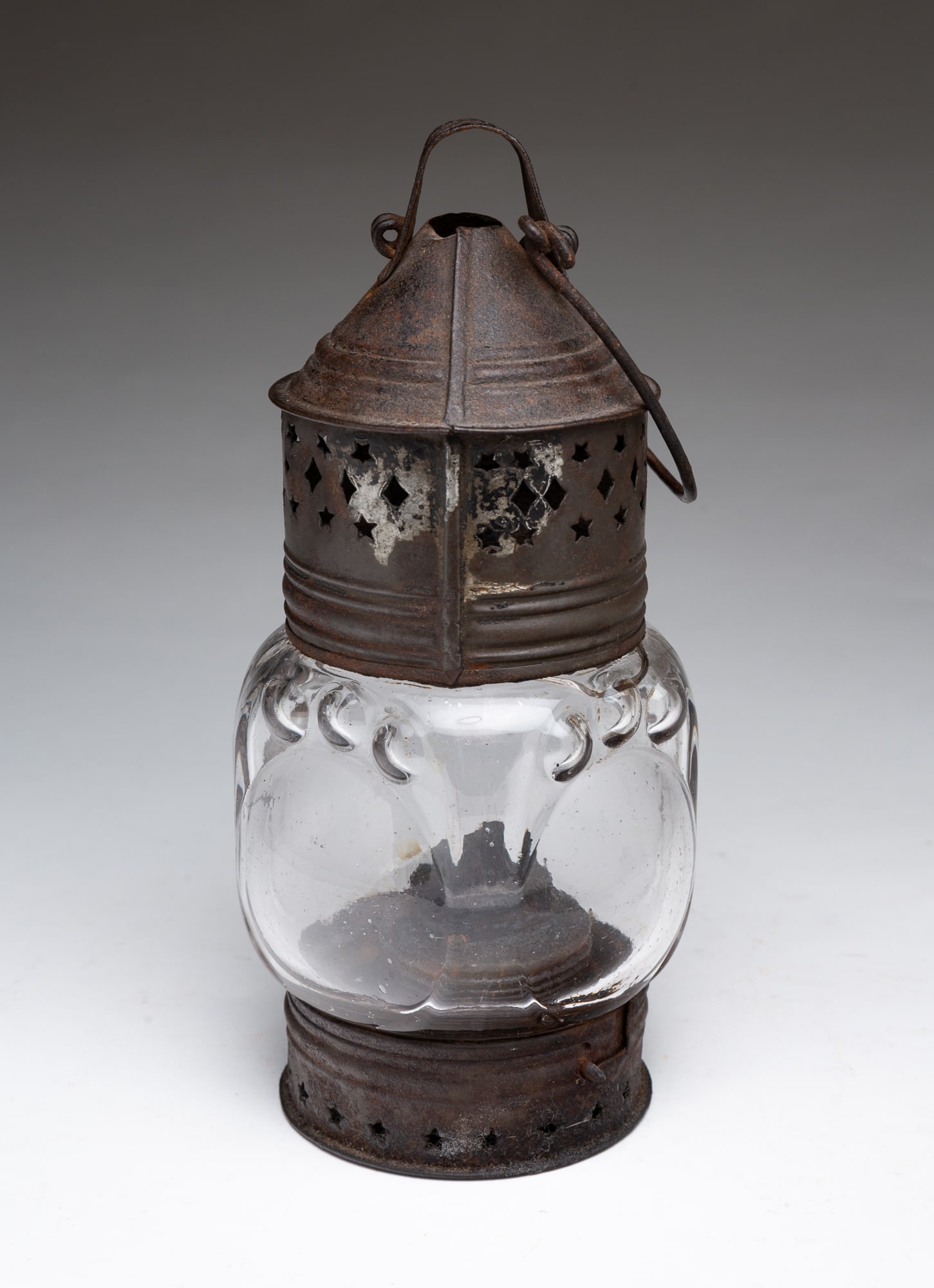 AMERICAN IRON AND BLOWN GLASS WHALE OIL LANTERN.: Mid-19th Century. Having an iron bale handle over conical iron top with pierced stars and diamonds, bullseye glass globe, double tube burner and glass font, iron base pierced with stars, base twists o