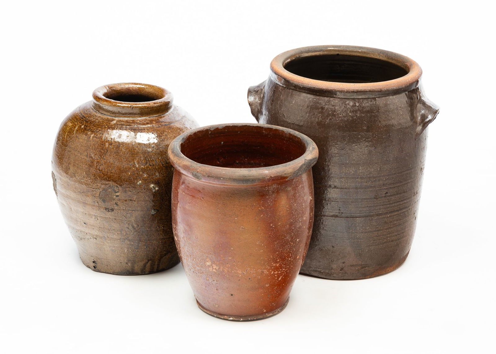 THREE AMERICAN STONEWARE VESSELS.: 19th Century. A southern glazed jar with dark glaze, spot of tobacco spit and a pronounced lip, 12.5"h. A redware jar with tapered form, rolled lip and brown glaze, 11.25"h. And a large jar with incis