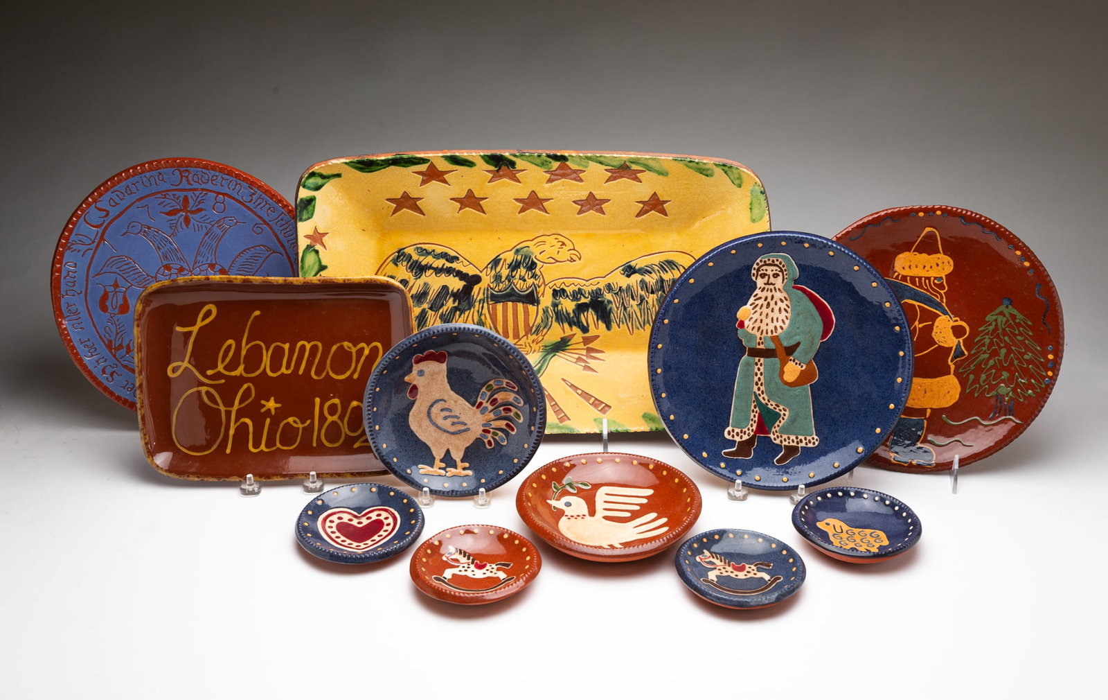 GROUP OF AMERICAN DECORATED REDWARE, INCL. TURTLE CREEK POTTERS (MORROW, OHIO).: 20th-21st Century. A rectangular "Lebanon Ohio 1802" platter by Liberty Pottery, 10"w. A round museum reproduction "Joined Birds" decorated redware platter, 10.25"w. Seven plates with vibrant animal
