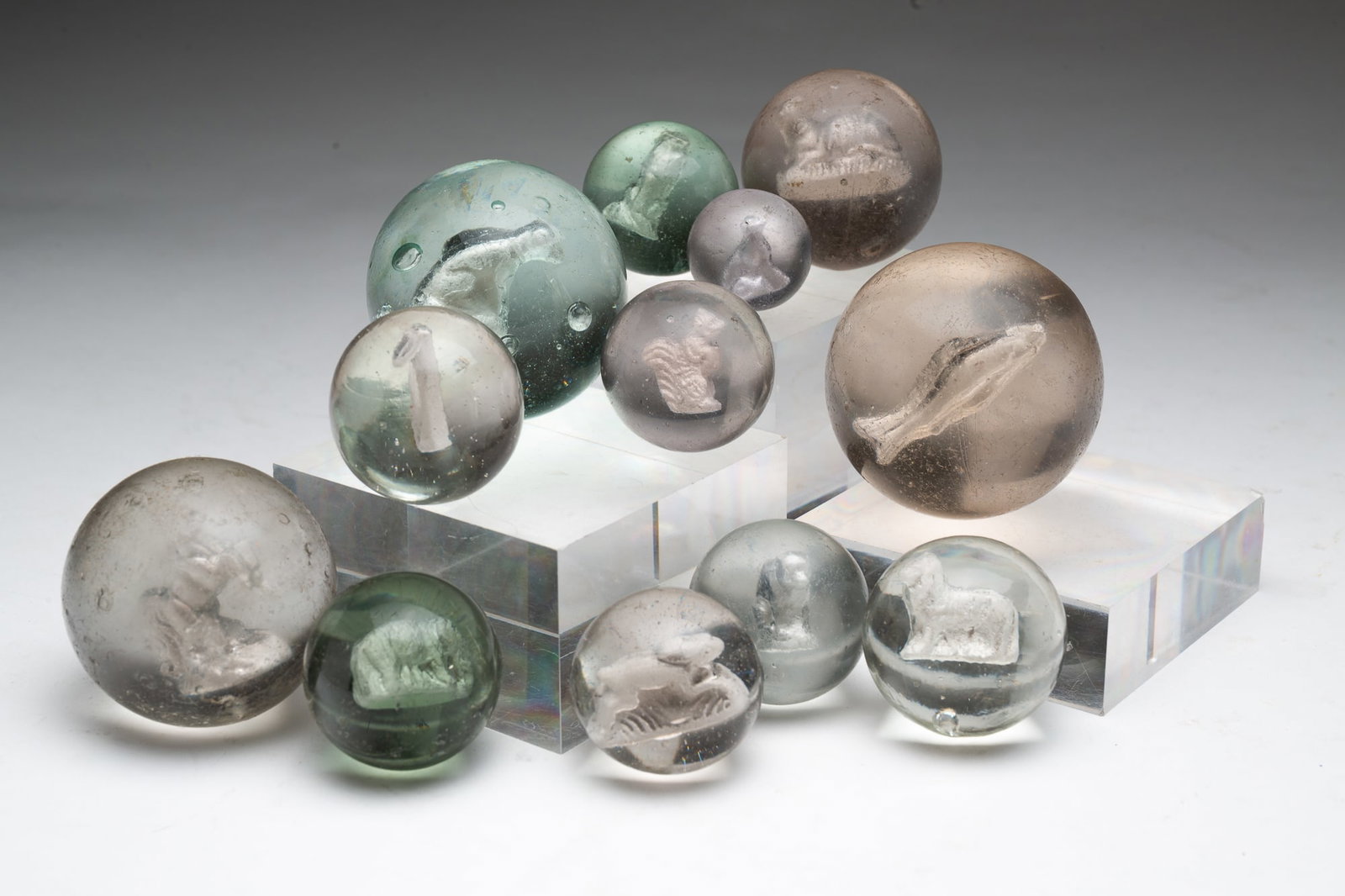 TWELVE GERMAN CLEAR GLASS SULFIDE MARBLES.: Ca. 1900. Mostly all animals, including cats, ribbits, dogs, a lamb, a squirrel, and others. Range in size from 2.5"d. to 1"d.Provenance: From the Lifetime Collection of the late Deb Fisher (Lebanon,