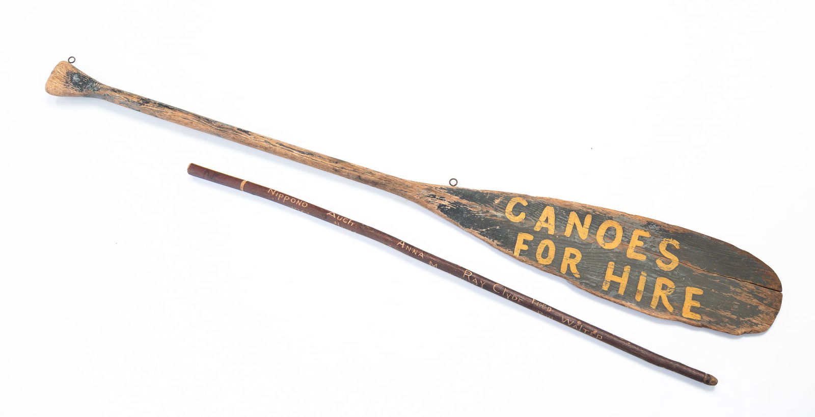 AMERICAN "CANOES FOR HIRE" PAINTED OAR TRADE SIGN PLUS FOLK ART "CAMP WEE WIN" CARVED CANE, DATED: 20th Century. Wood. The oar retaining remnants of black and grey paint while the paddle has yellow letters reading "CANOES / FOR HIRE". The top edge is fitted with two ring hangers. The cane is carved