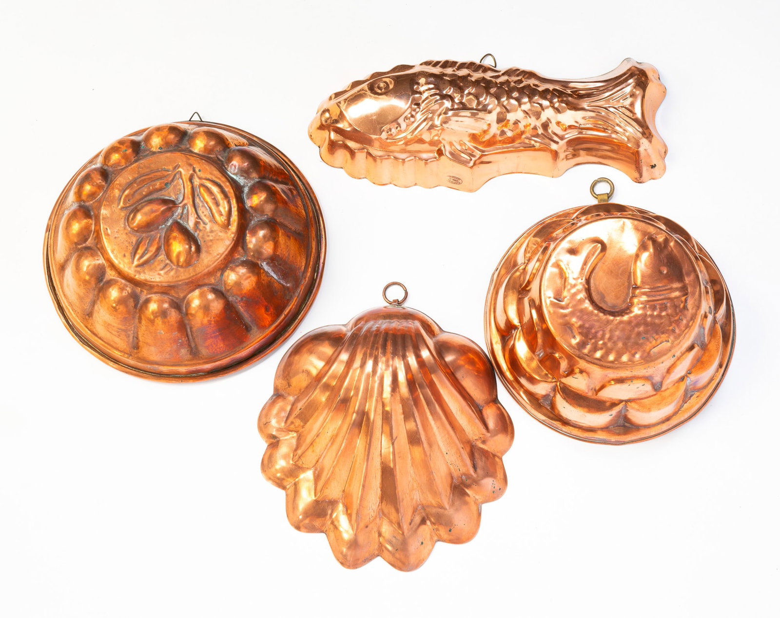 FOUR EUROPEAN COPPER FOOD MOLDS.: 19th Century. Comprising a fish-form example, a shell-form mold, a round example with a hanging fruit design, and a round mold with a fish design; hanging fruit design having a copper interior and the
