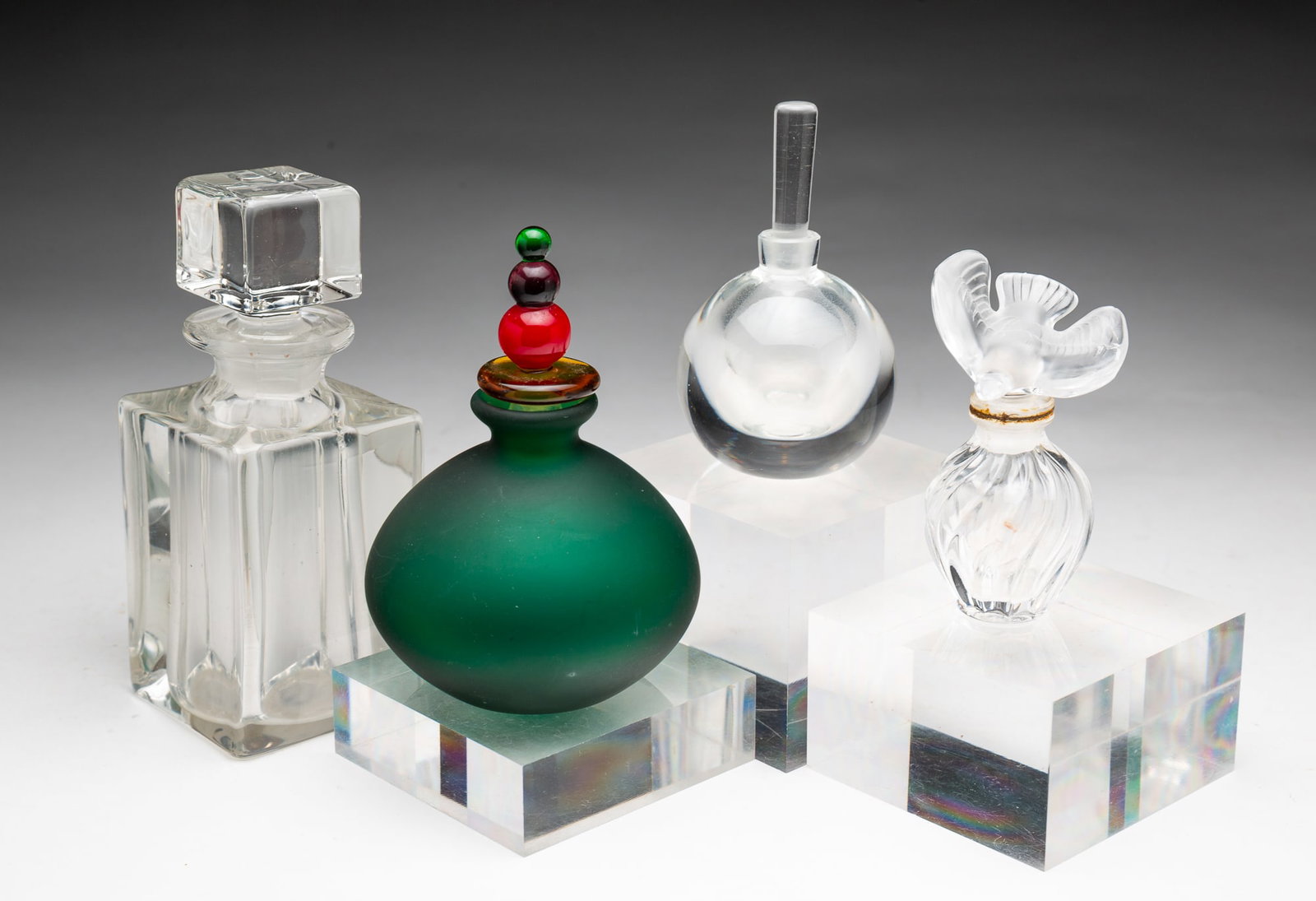 FOUR EUROPEAN PERFUME BOTTLES, INCL. LALIQUE.: 20th Century. Comprising a miniature Lalique swirl bottle with dove-form topper, signed; an Orrefors crystal globular bottle with stopper, signed "Sweden; a square-form bottle with square-form stopper