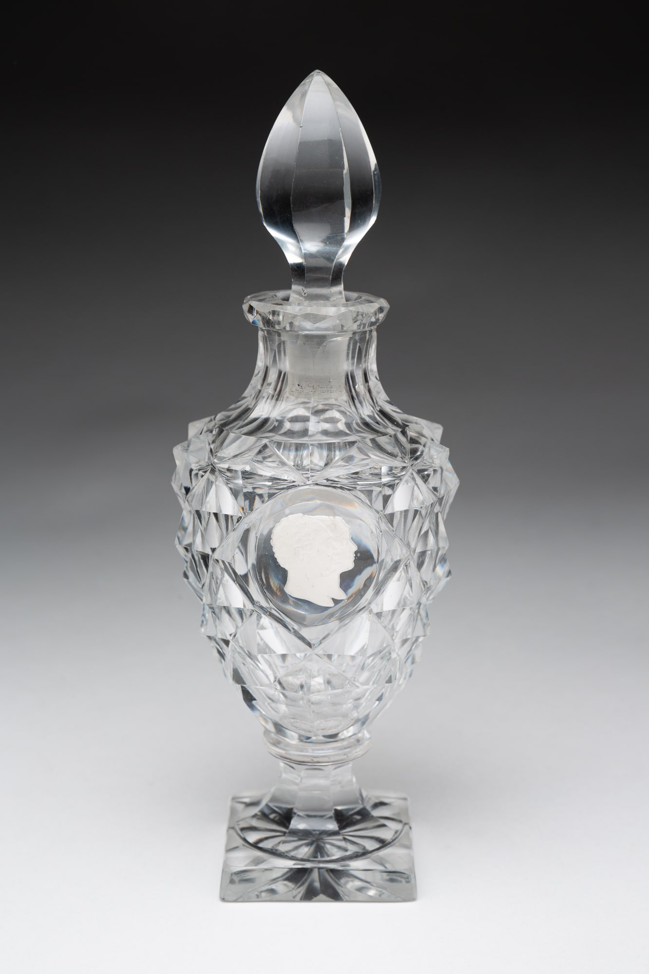 CUT GLASS COLOGNE WITH SULFIDE BUSTS.: European, 19th Century. Square foot with starburst, paneled stem wafered to sawtooth cut bottle, double sulfide busts and panel cut replaced stopper. 7.75"h.