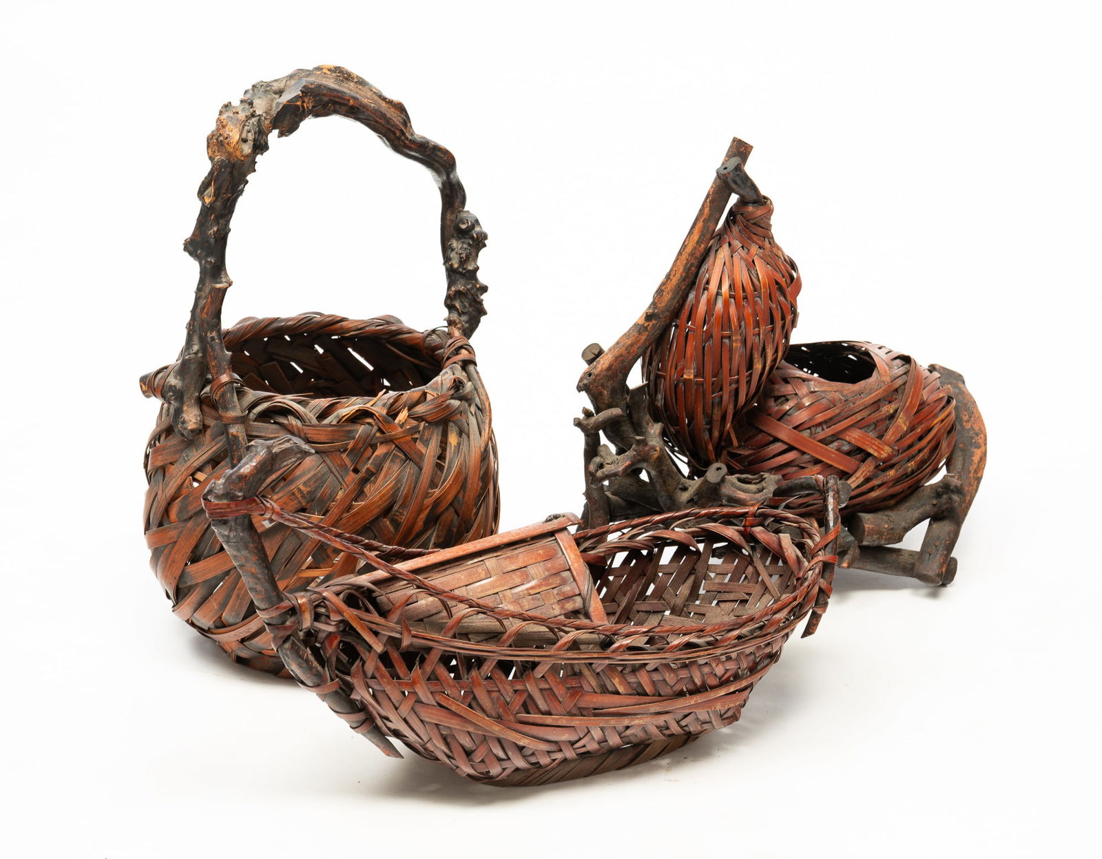 THREE JAPANESE WICKER AND BAMBOO IKEBANA BASKETS.: Early 20th century. Large carrying basket with wood handle. 16"h. 5.5"d. Medium basket cradled in a wooden base. 14"h. 14"l. Small flower basket in a classic boat design. 10"h. 17"l.