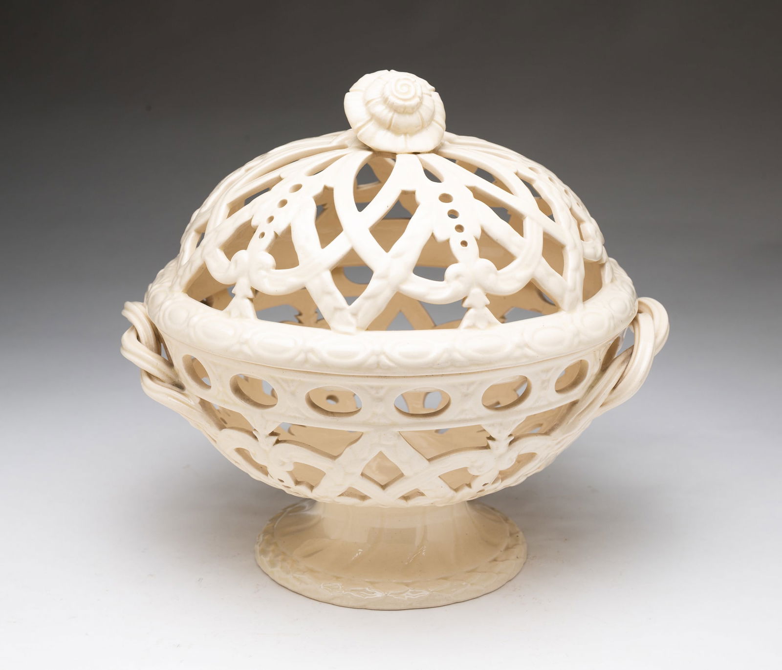 WEDGWOOD CREAMWARE RETICULATED COVERED ORANGE BASKET.: English, 19th Century. Of circular form, a large covered openwork basket, the lid topped with a floral finial, the body having twisted handles and raised on a pedestal with circular, having impressed