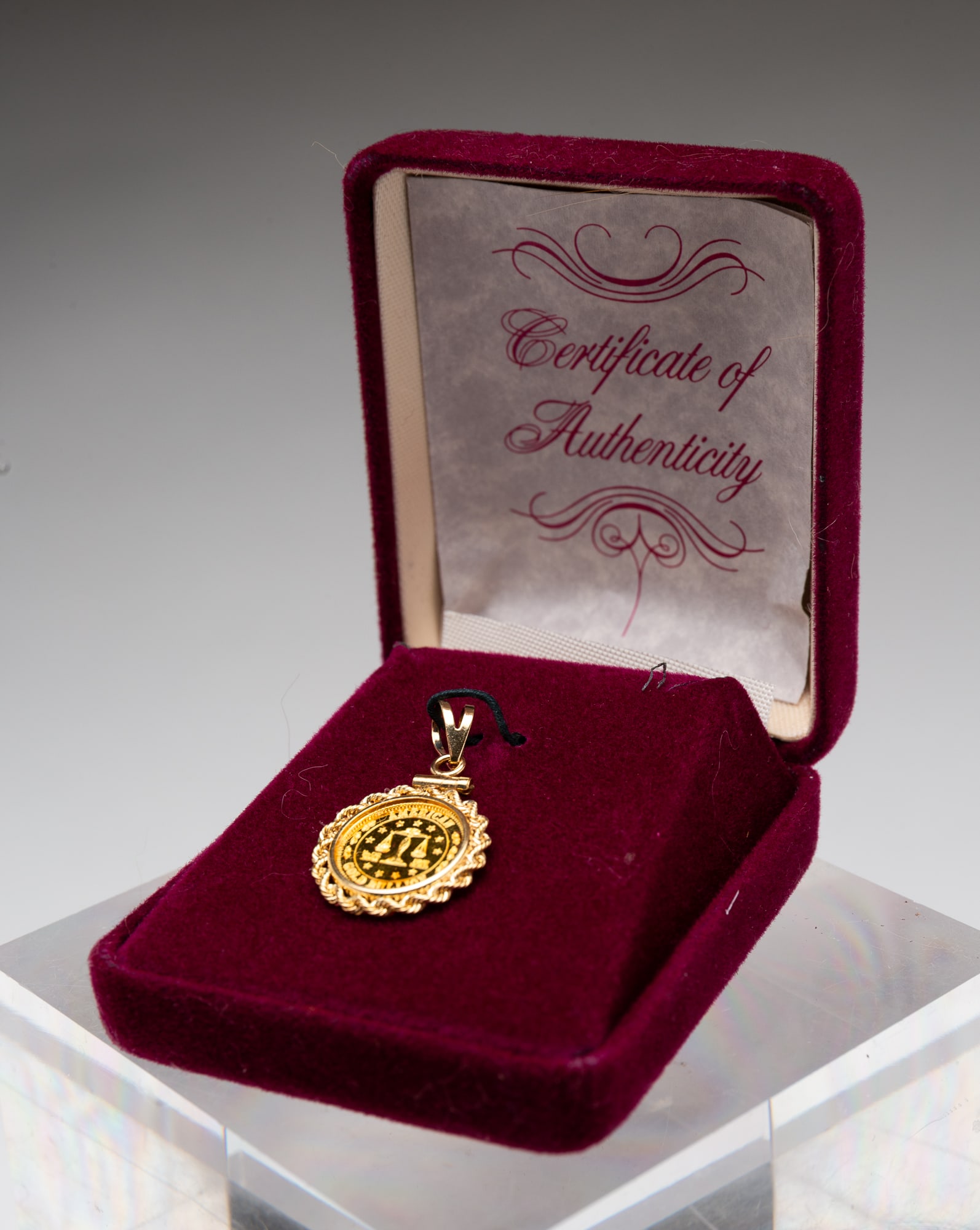 AMERICAN 24K GOLD BOUILLON PENDANT.: Dated 1987. A 1/20th oz. 24K gold bouillon coin in a 14K gold rope twist bezel. Approximately 3.10g.