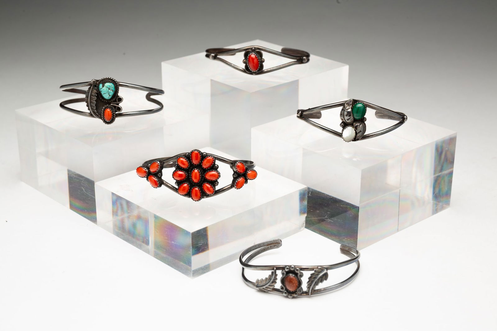 FIVE STERLING SILVER NAVAJO TURQUOISE AND CORAL CUFFS.: Native American, 20th Century. A leaf motif cuff set with a coral cabochon and a turquoise stone, a leaf motif cuff with a central sunstone cabochon, one with a singular coral cabochon, a leaf motif c