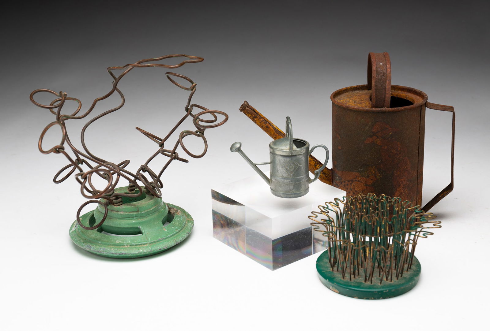 TWO METAL FLOWER FROGS AND TWO MINIATURE WATERING CANS, INCL. BLUE RIBBON FLOWER HOLDER CO.: American, 20th Century. Flower holder on a weighted green metal base with several crimped wires, signed "Blue Ribbon Flower Holder Co., Cuyahoga Falls, O" on base. Flower holder on a green pierced
