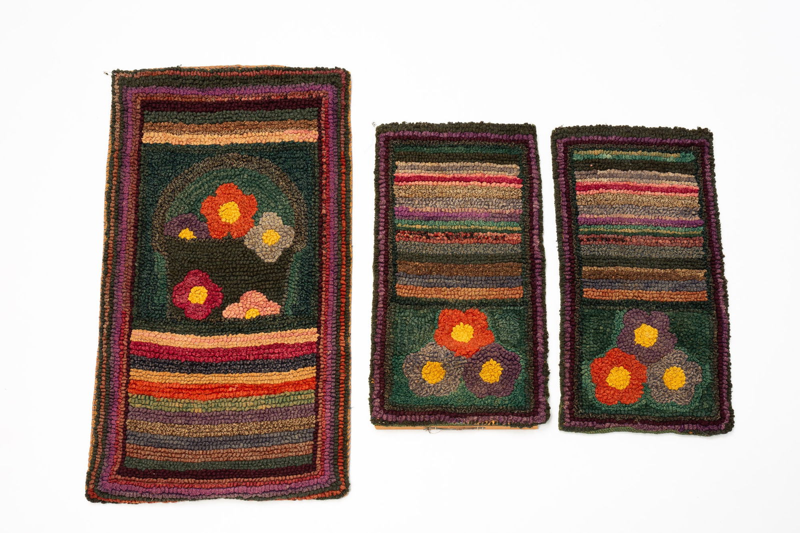 THREE CATHERINE AUGENSTEIN (MARION, OHIO) FLORAL HOOKED RUGS.: American, ca. 1900. Three rectangular mats in similar patterns. Largest with multiple striped borders, center with flowers above a group of lines. As well as two smaller examples in a very similar