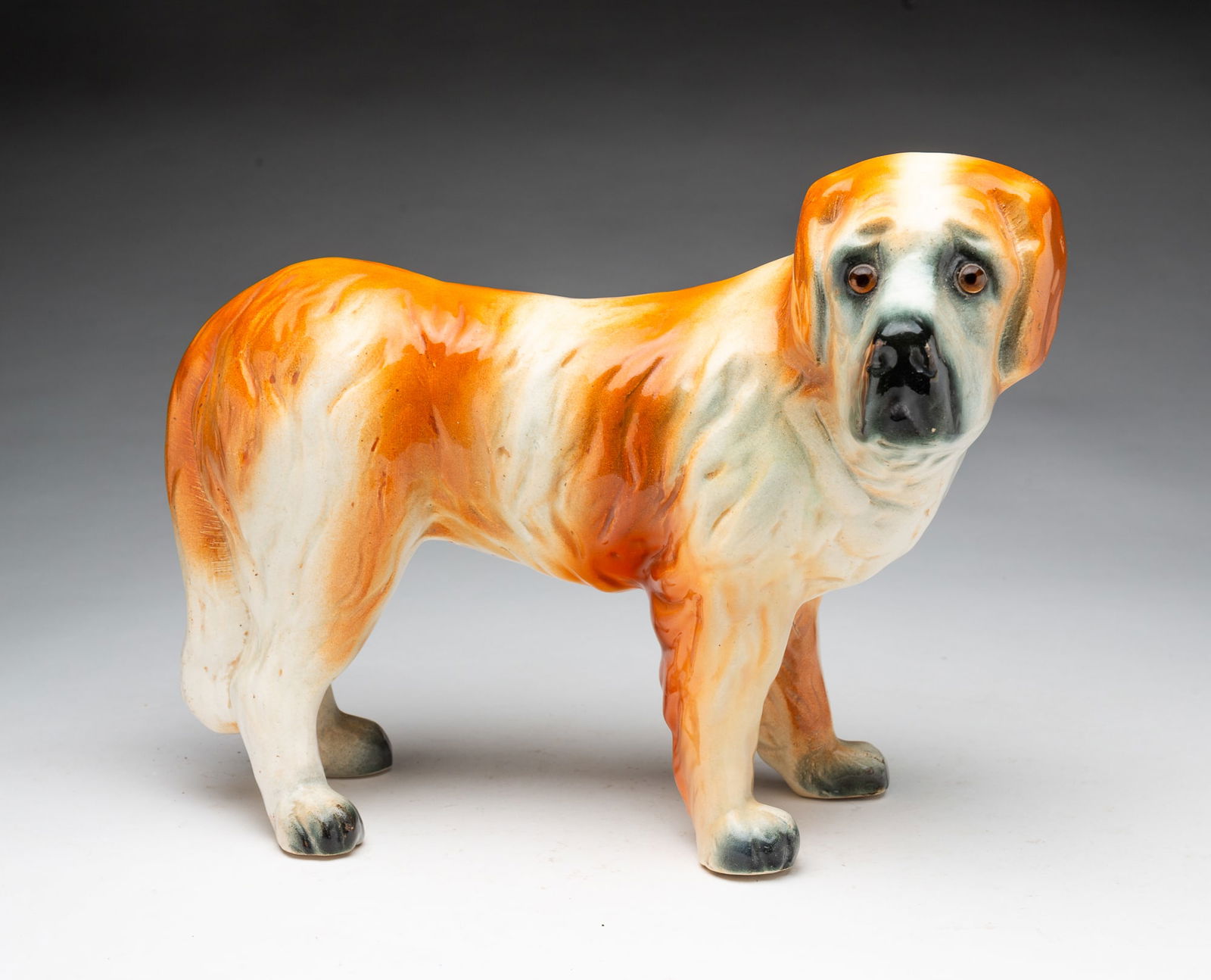 LARGE STAFFORDSHIRE FIGURE OF A ST. BERNARD.: English, Late 19th Century. Hand-painted St. Bernard in orange-brown and cream with black eye area, muzzle, and paws, having amber glass eyes and a somewhat forlorn facial expression.Provenance: From
