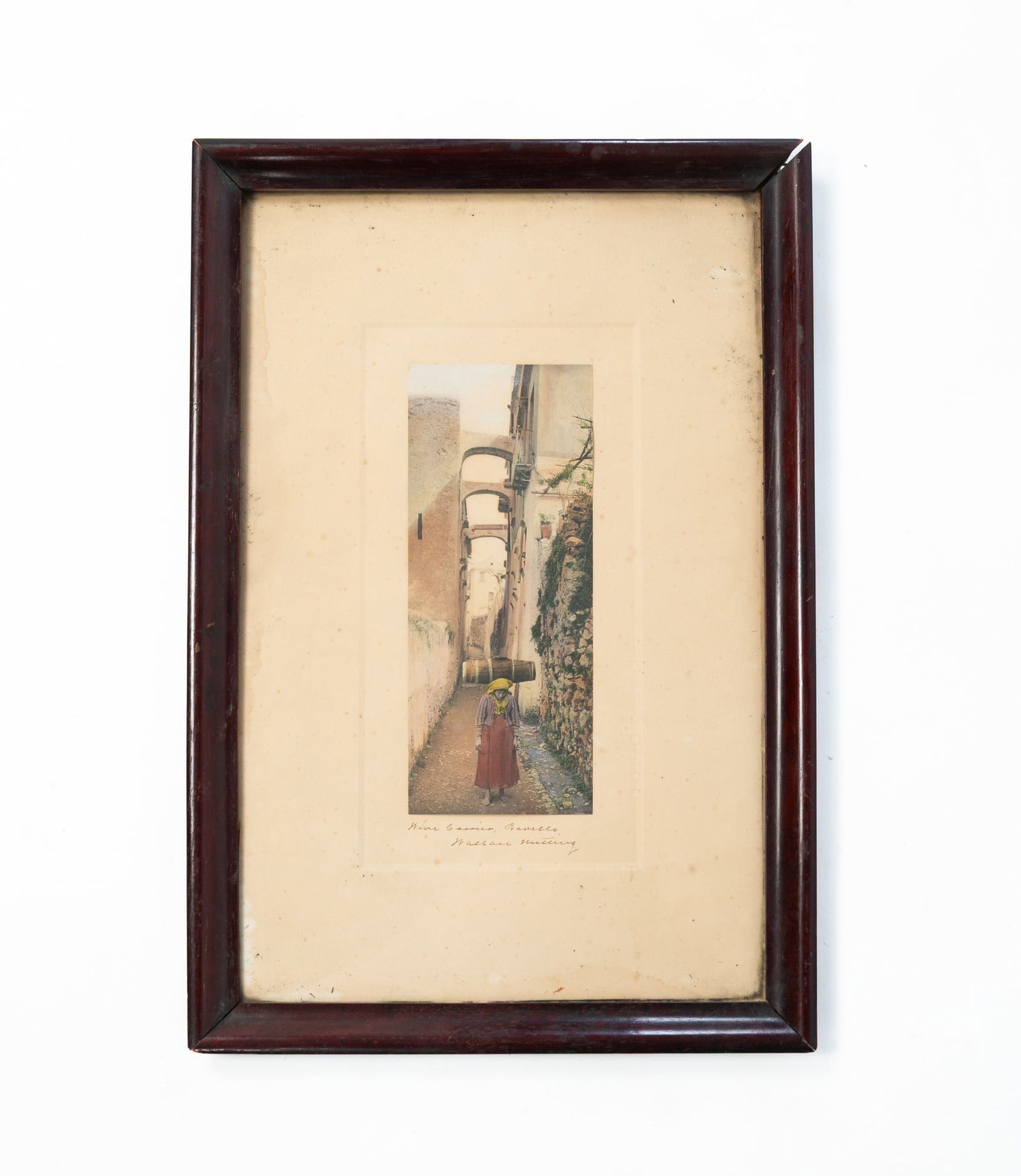 WALLACE NUTTING (AMERICAN, 1861-1941) "WINE CARRIER, RAVELLO" PRINT.: Ca. 1900. Woman walking down an alley titled "Wine Carrier, Ravello". Titled and signed to bottom. Matted in a wood frame behind glass. Frame 18.5"h. 12.5"w.