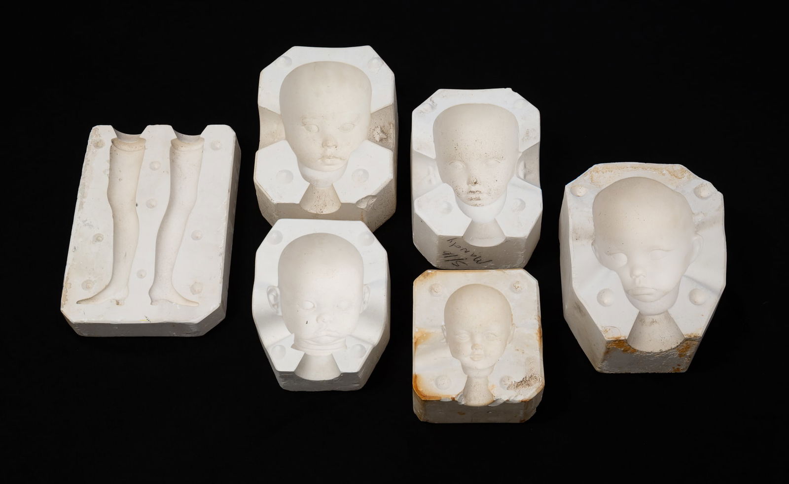 GROUP OF PLASTER DOLL MOLDS.: American, 20th Century. Five head molds in varying sizes and a mold with two legs. Few marked "The Ultimate Collection", "Lasting Impressions", and "The Doll Artworks".Provenance: From the Lifetime